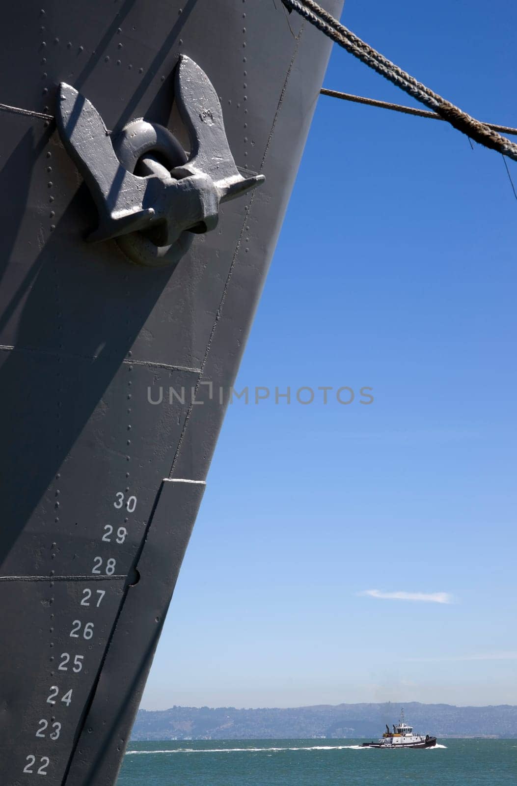 Vertical Composition of Moored Ship Bow and Anchor Tugboat Passing in Bay Underneath