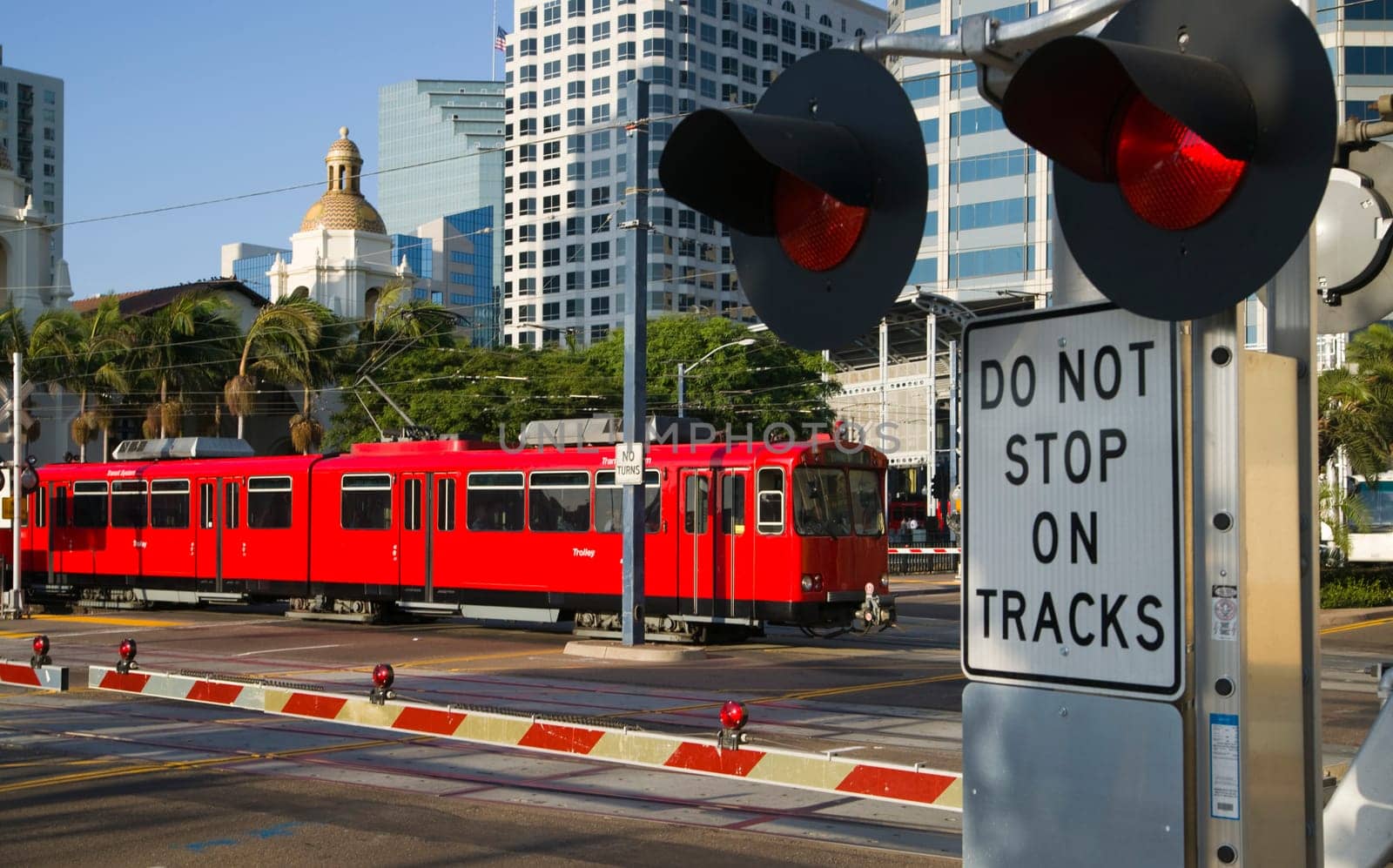 Downtown Scene at RailRoad Crossing Red Trolley Car Passing Signal Lights with Buildings in the Background