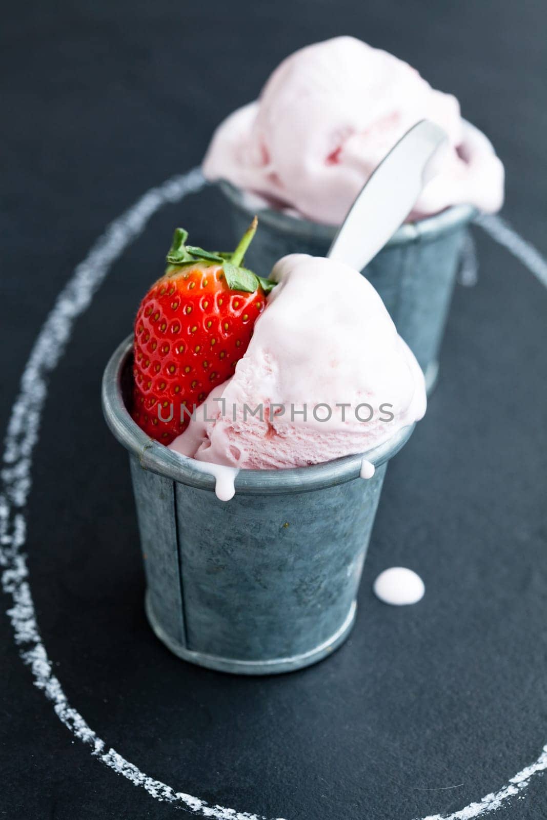 Closeup of strawberry ice cream and strawberry in two metal cups inside chalk circle on dark background