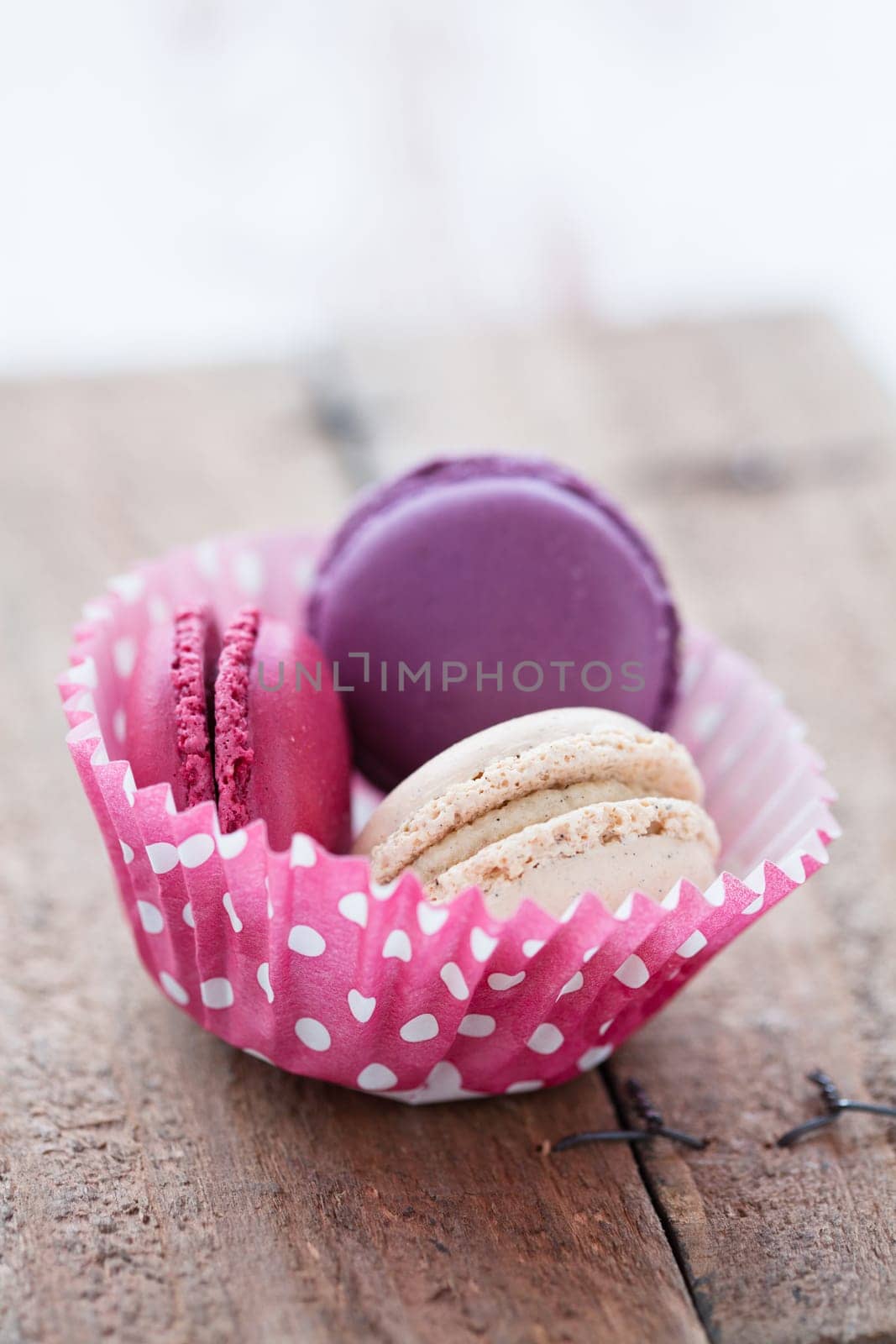 Closeup of three different flavoured macaroons in paper cupcake cup on wooden table