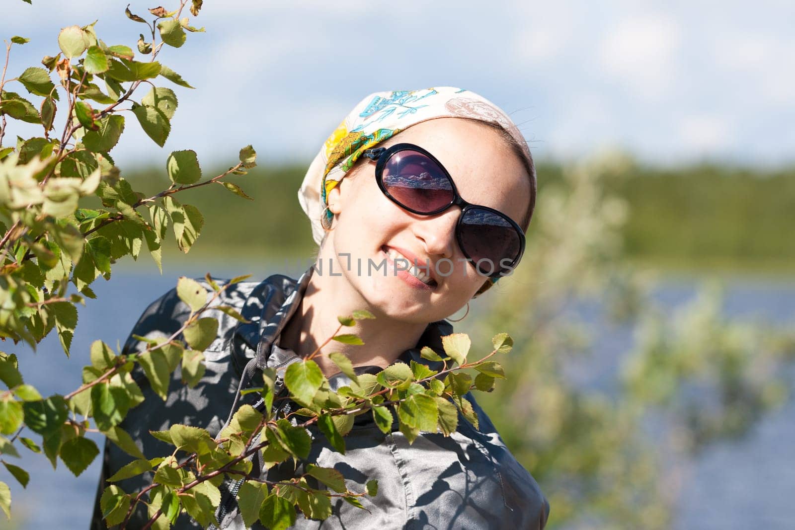 beautiful girl in a bandana and sunglasses looks out from behind the bushes on a sunny day