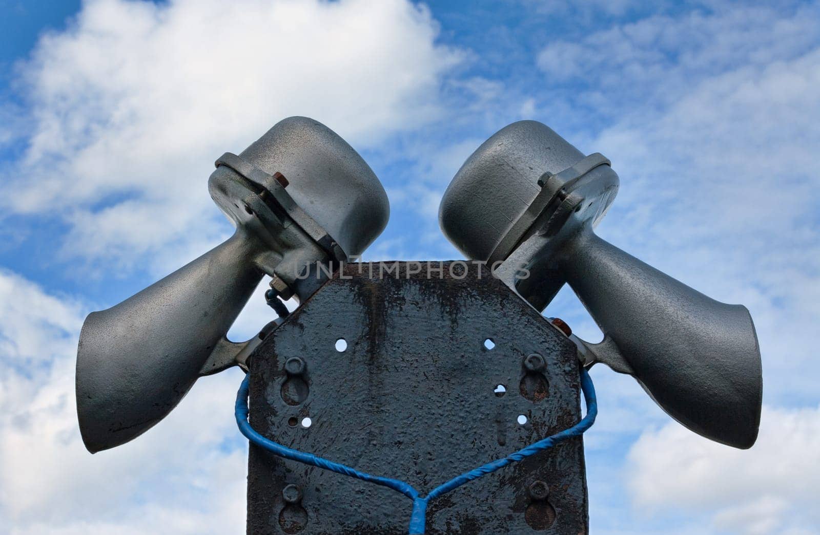 A pair of loudspeaker megaphones mounted atop a tall pole set against a cloudy blue sky.