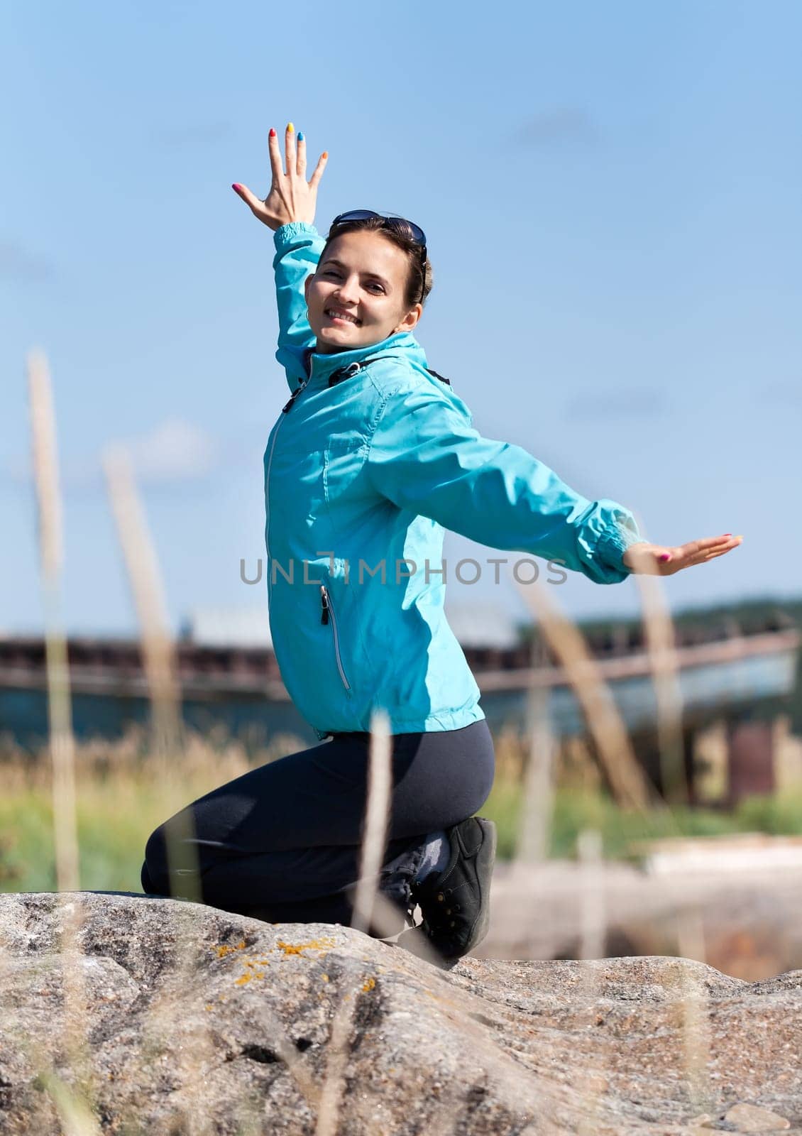 Beautiful girl in a jacket kneeling on a rock, enjoying life and the wind.