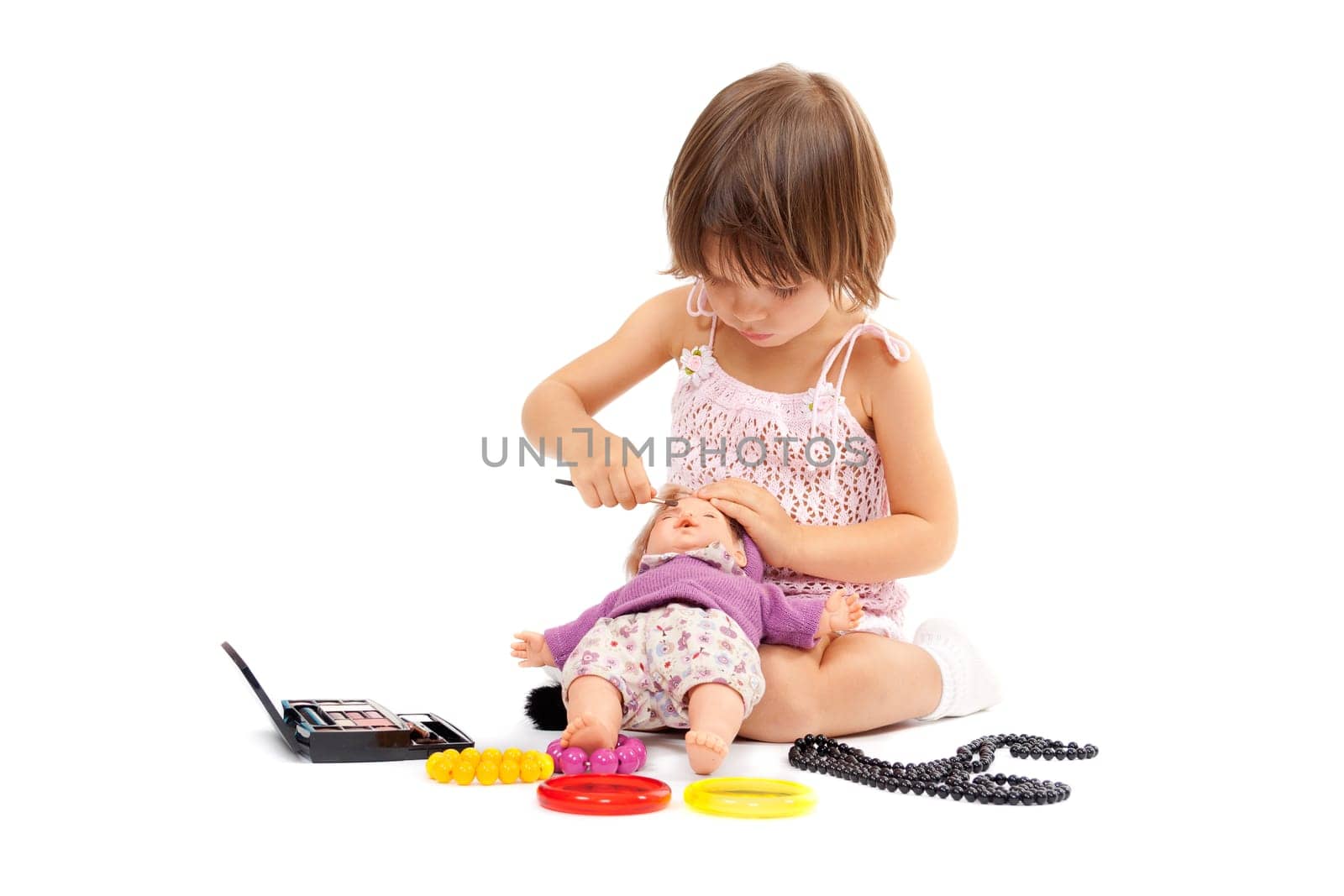 Beautiful little girl paints cosmetics doll. Studio concept. Isolate on white.