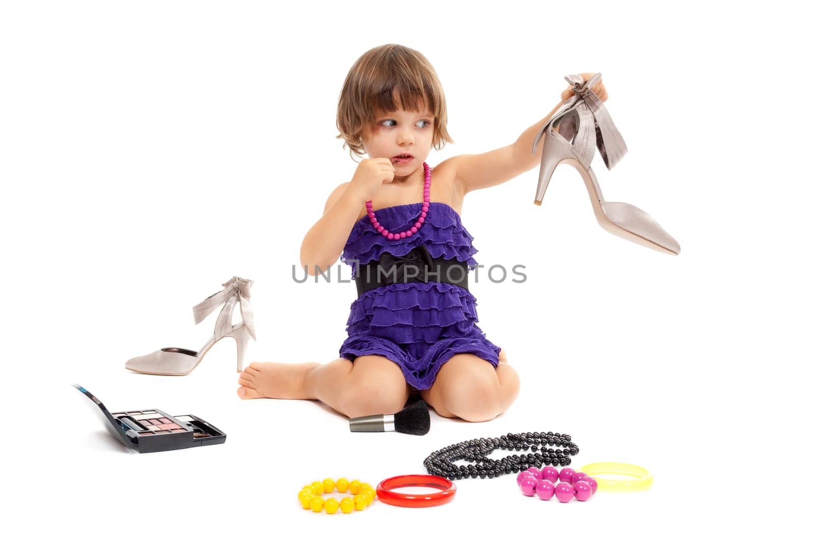 Cute little girl with cosmetics and women's shoes in the studio. Isolate on white.