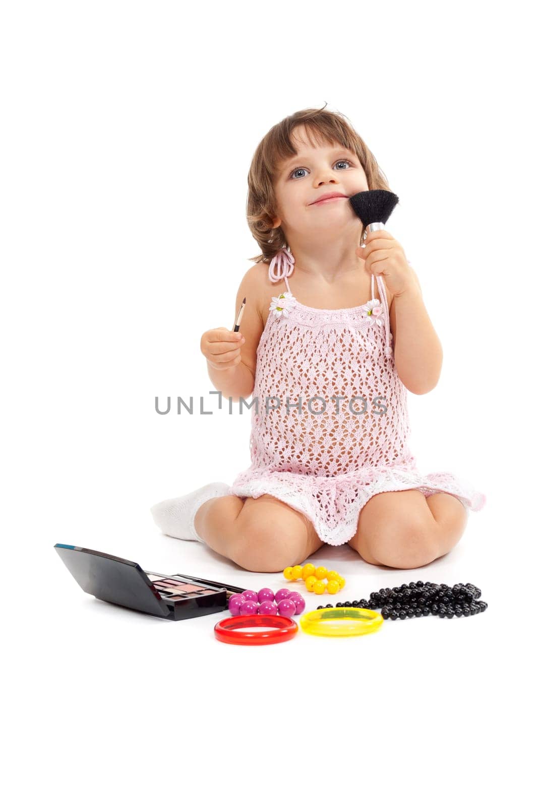 Charming little girl with makeup and colored beads in the studio sitting on the floor. Isolate on white.