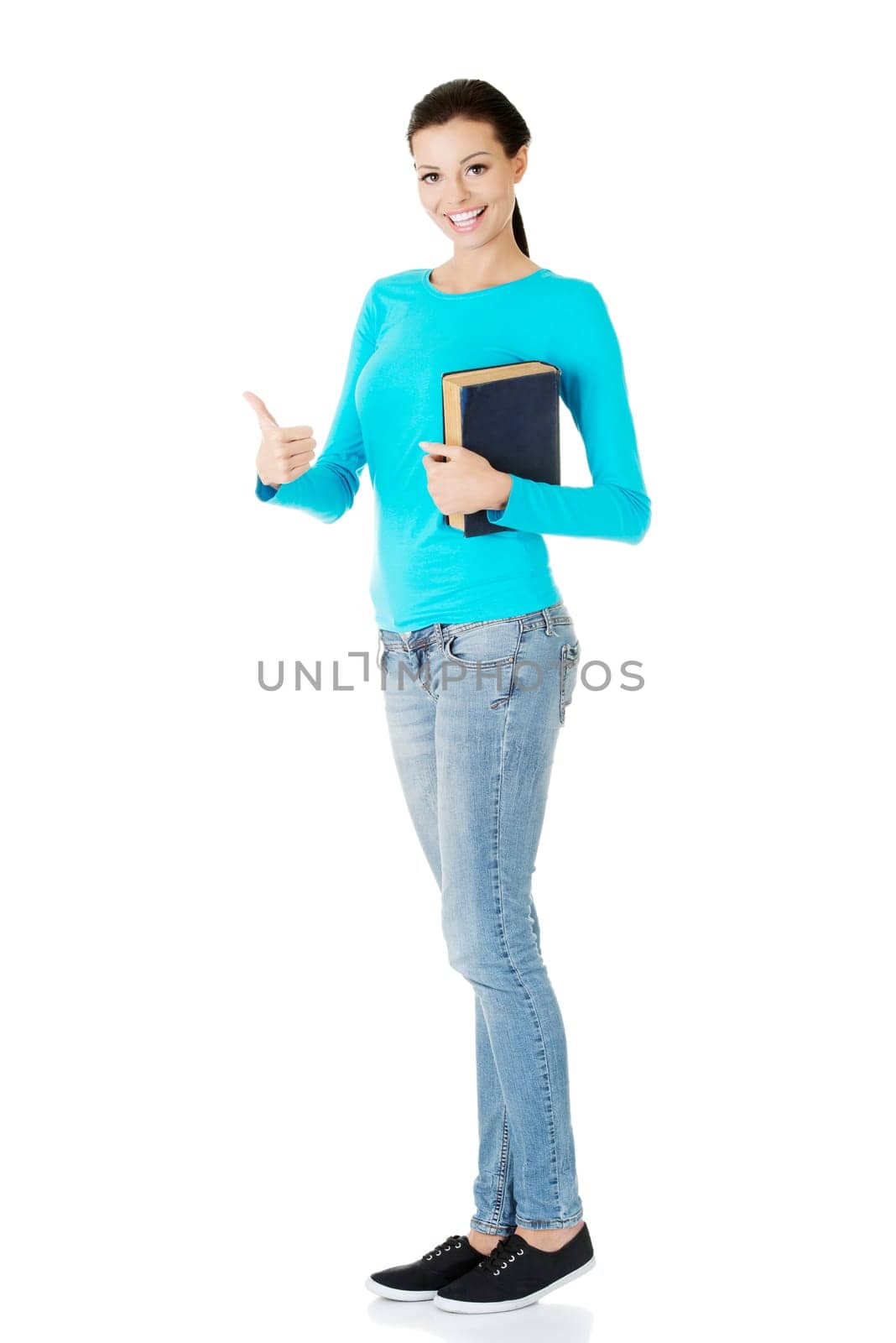 Attractive young student woman with book gesturing OK, isolated on white