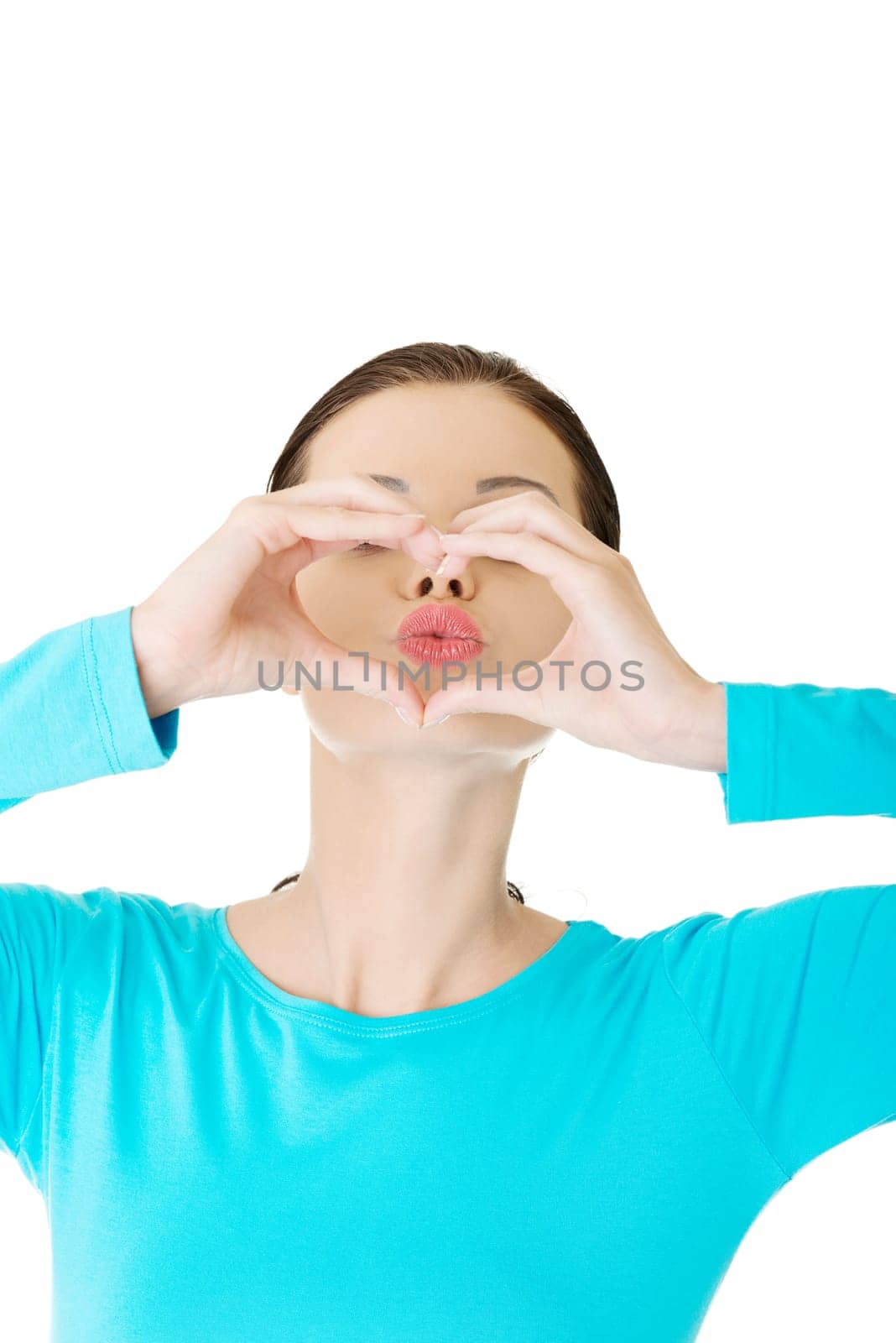 Attractive young woman showing heart gesture with hands and sending kiss