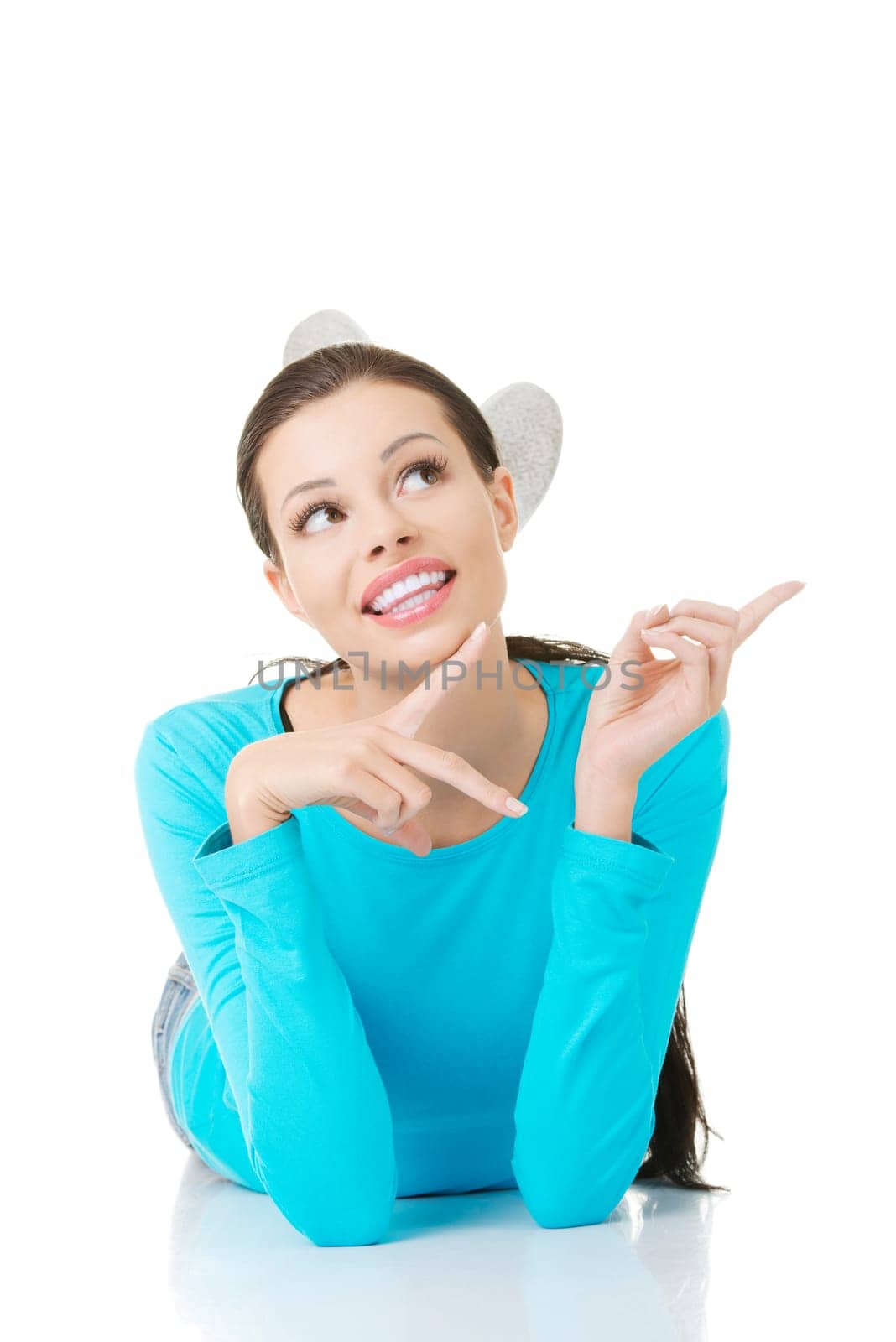 Young beautiful happy woman in casual clothes lying on floor and pointing on copy space, isolated on white