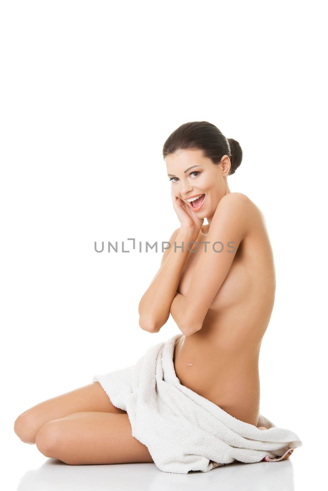 Young happy naked woman covering her self with towel on white background.