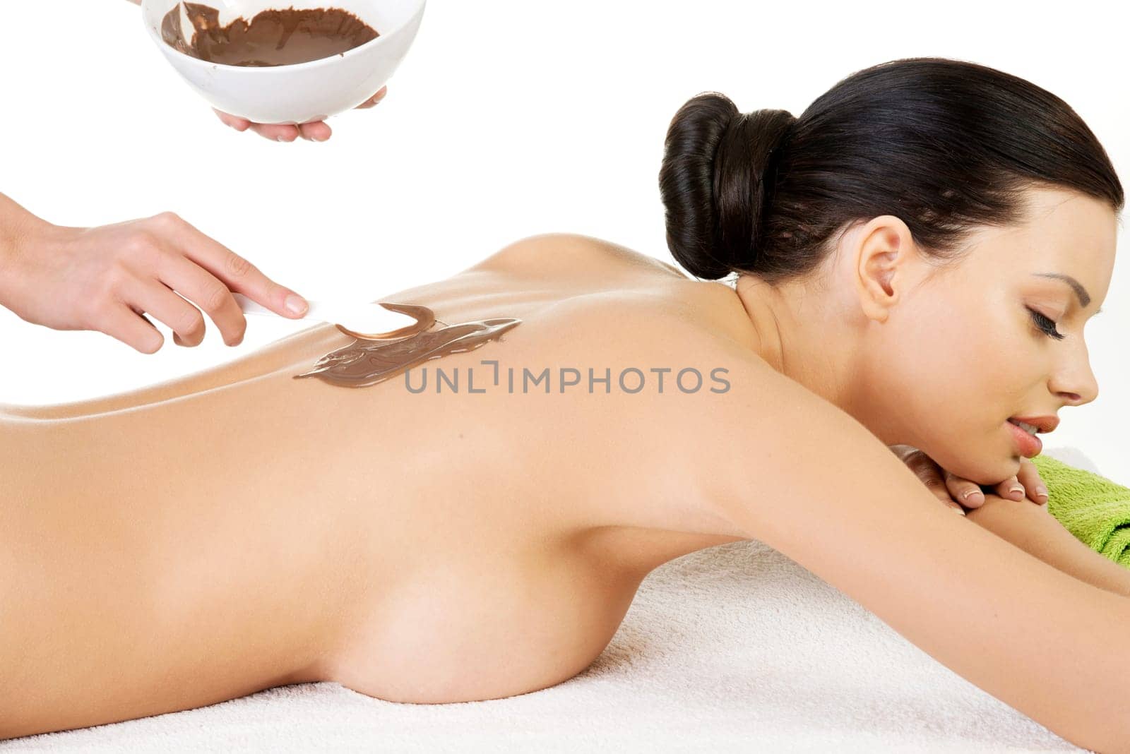Pretty young woman relaxing being massaged in spa saloon with chocolate. Isoalted on white