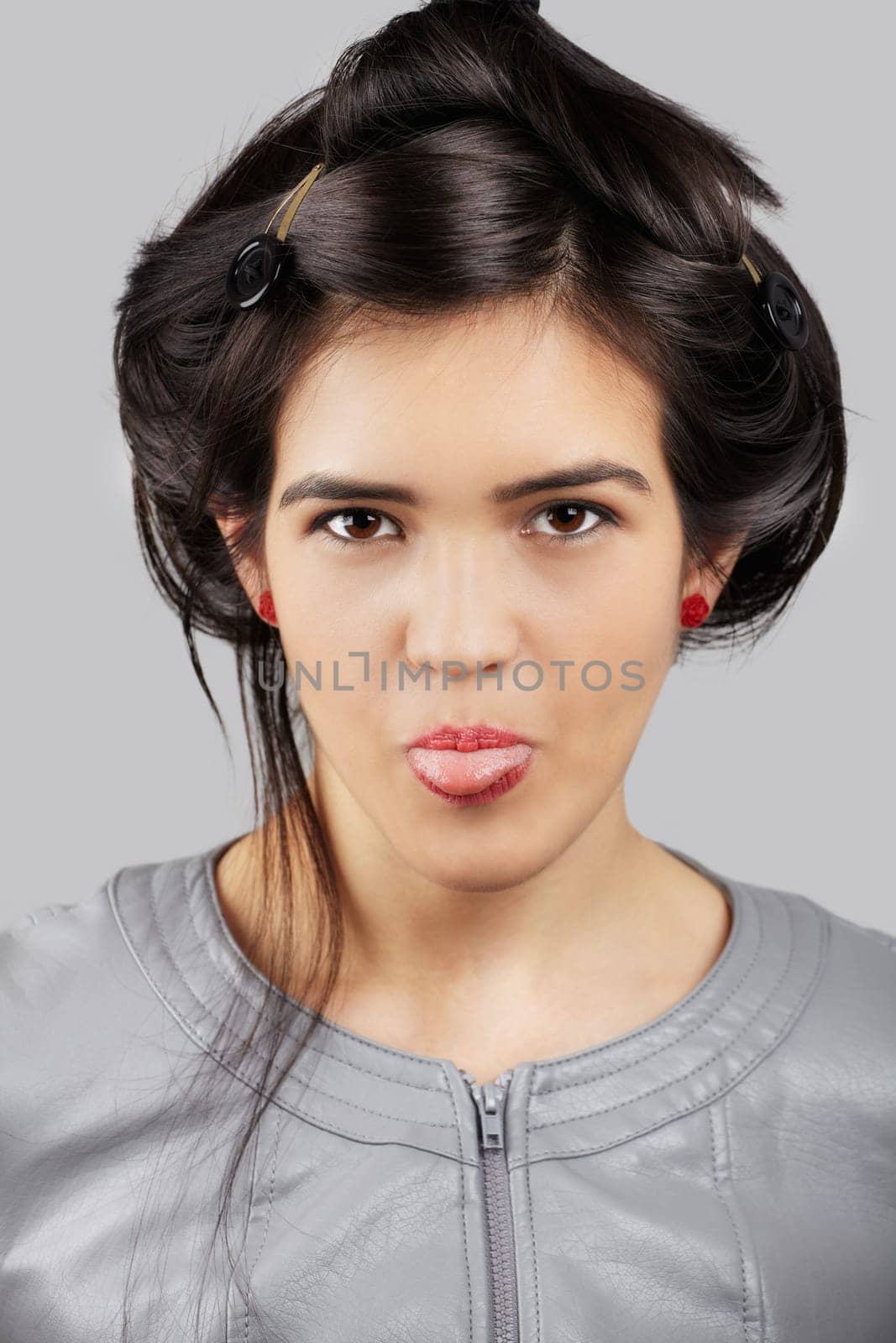 Young asian woman sticking out her tongue out isolated on grey background.