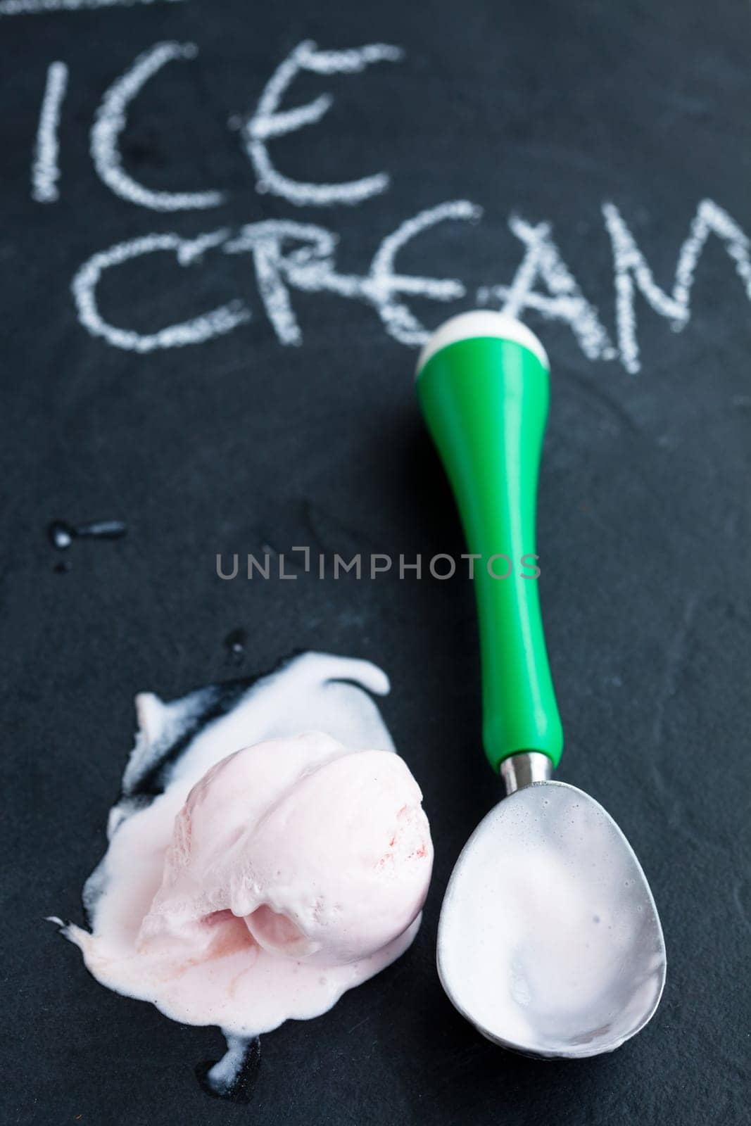 Closeup of strawberry ice cream and scoop on dark background with text written in chalk
