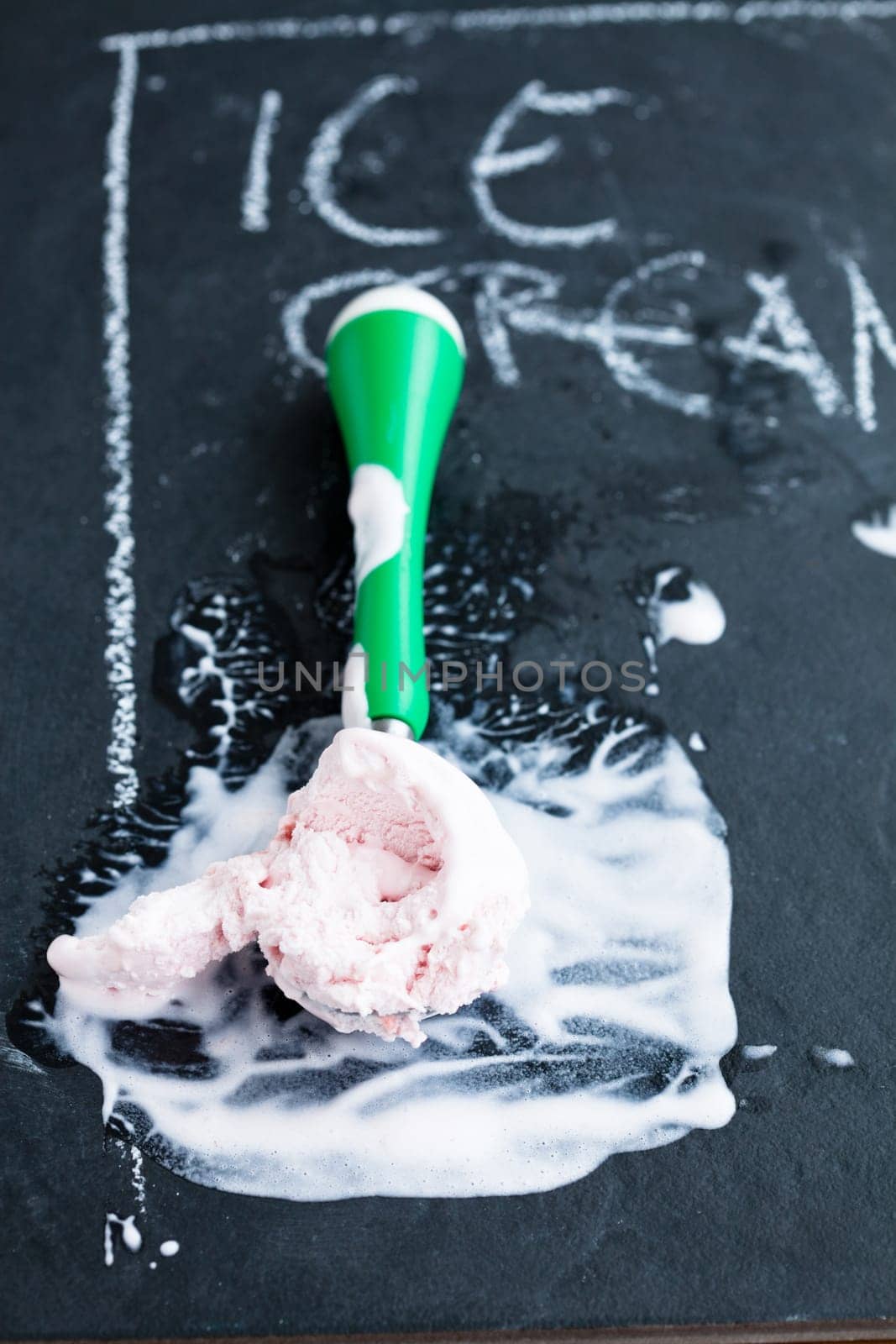 Closeup of strawberry ice cream and scoop on dark background with text written in chalk
