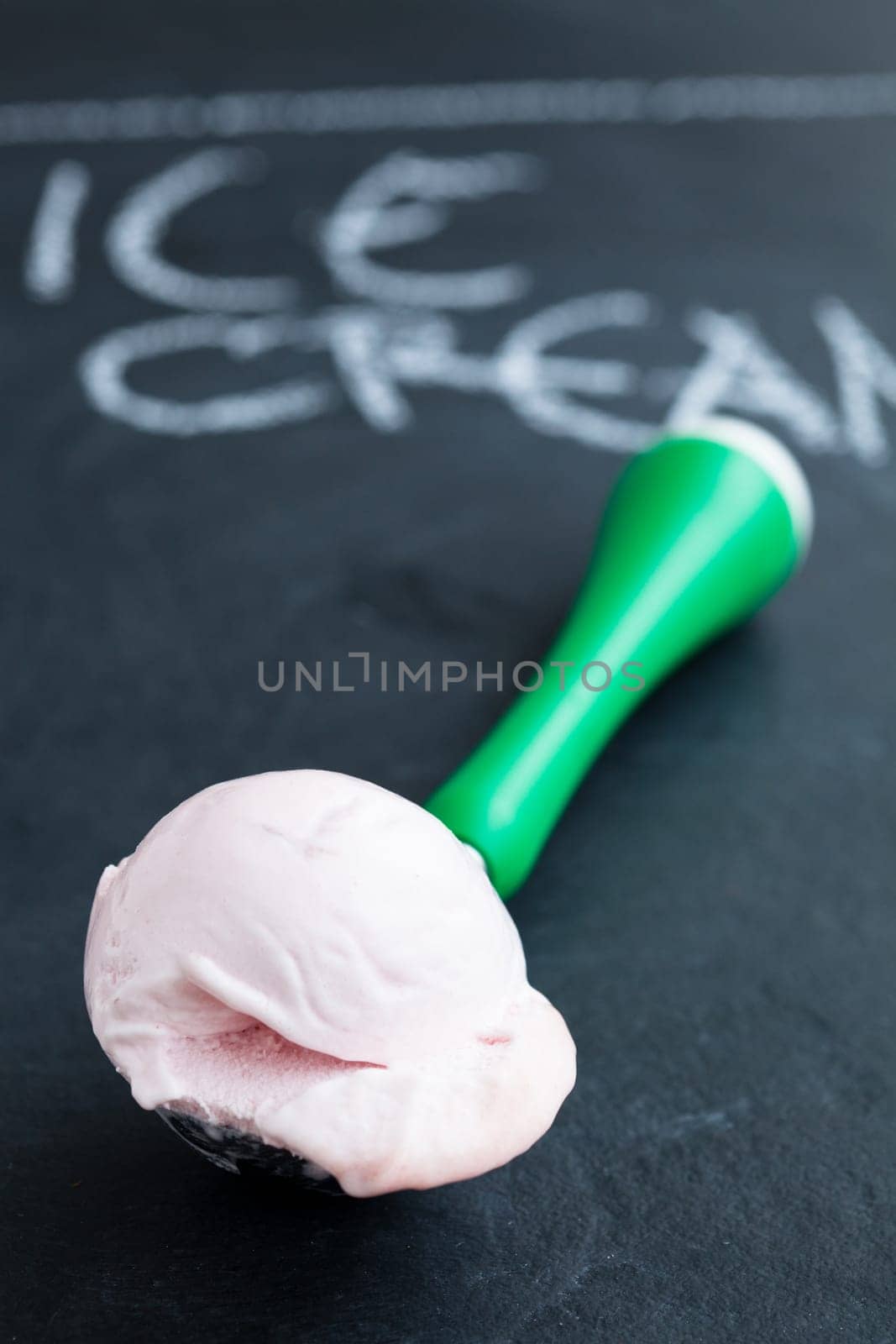 Closeup of strawberry ice cream and scoop on dark background with text written in chalk