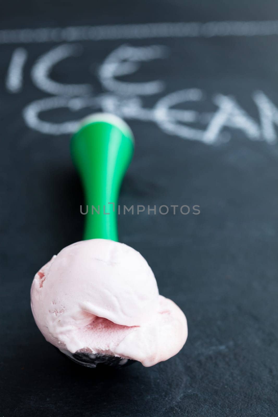 Closeup of strawberry ice cream and scoop on dark background with text written in chalk