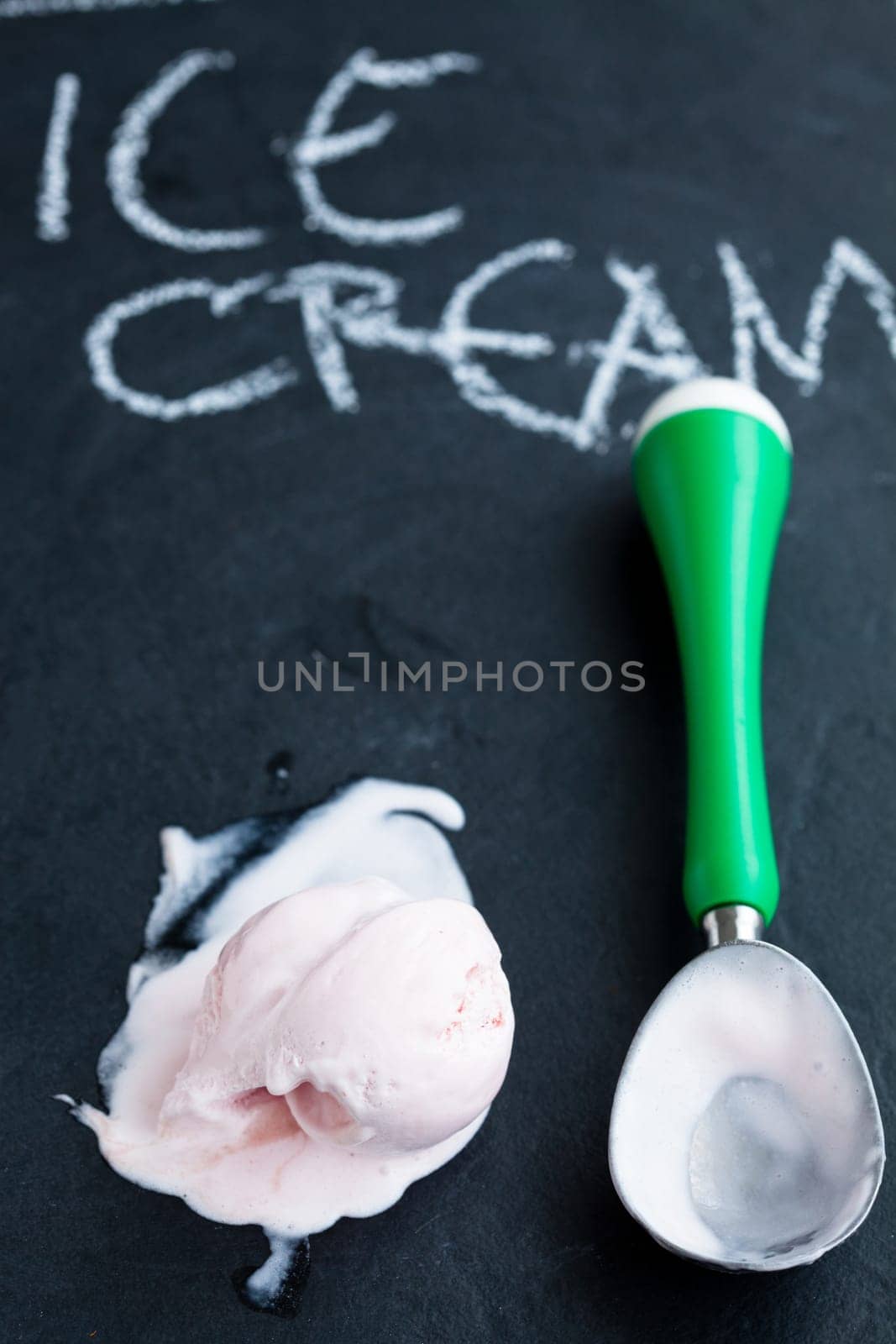 Closeup of strawberry ice cream and scoop on dark background with text written in chalk