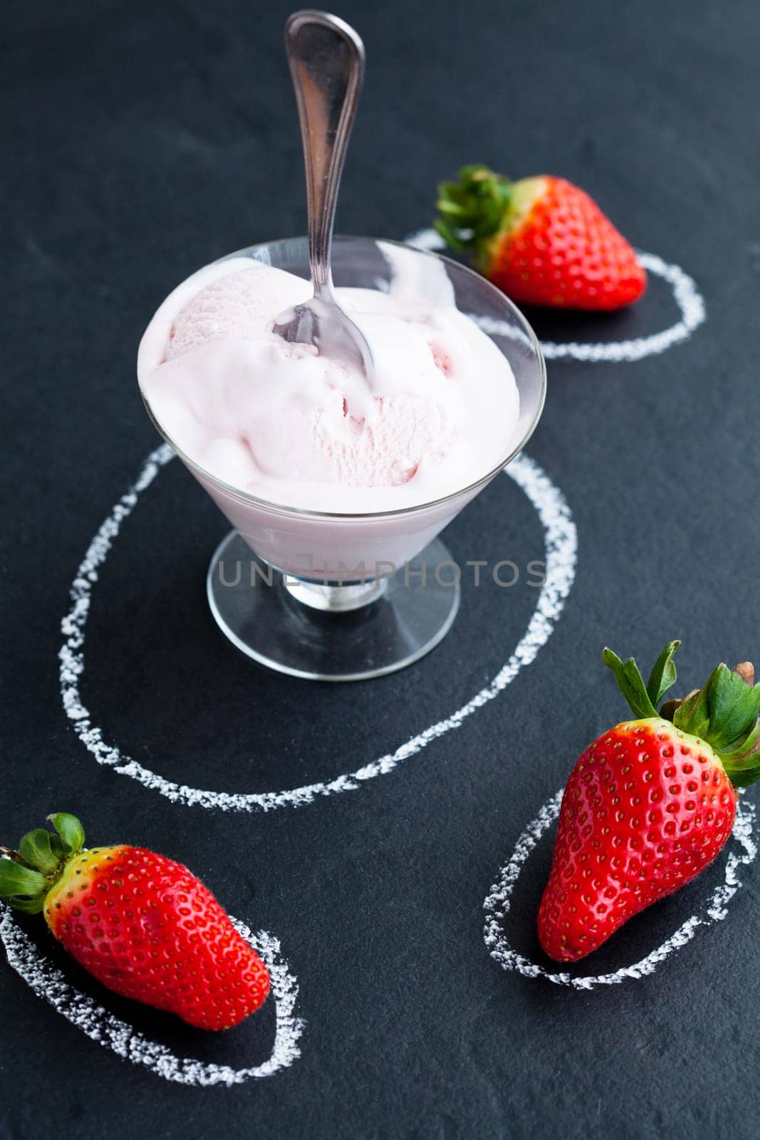Strawberry ice cream in glass bowl and three whole strawberry on dark background
