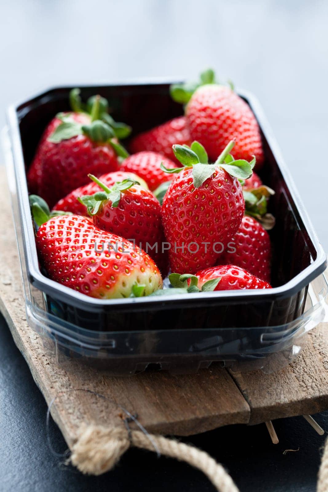 Fresh whole strawberries in plastic packing tray on wooden surface