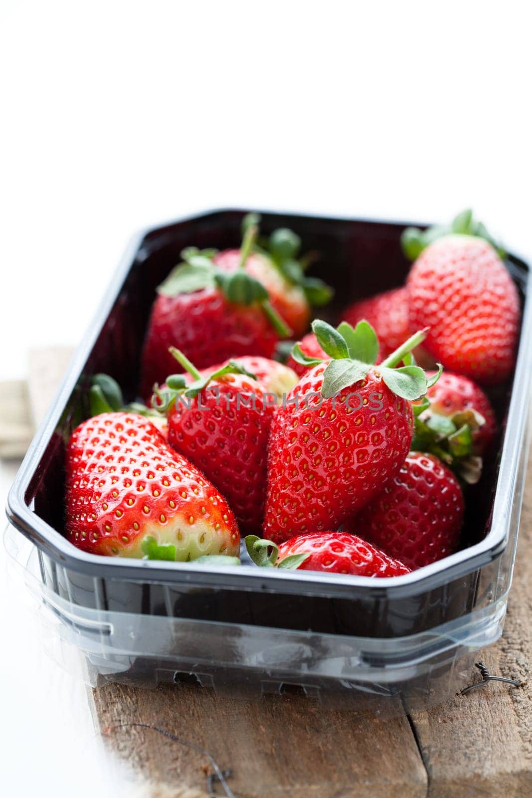 Fresh whole strawberries in plastic packing tray on wooden surface