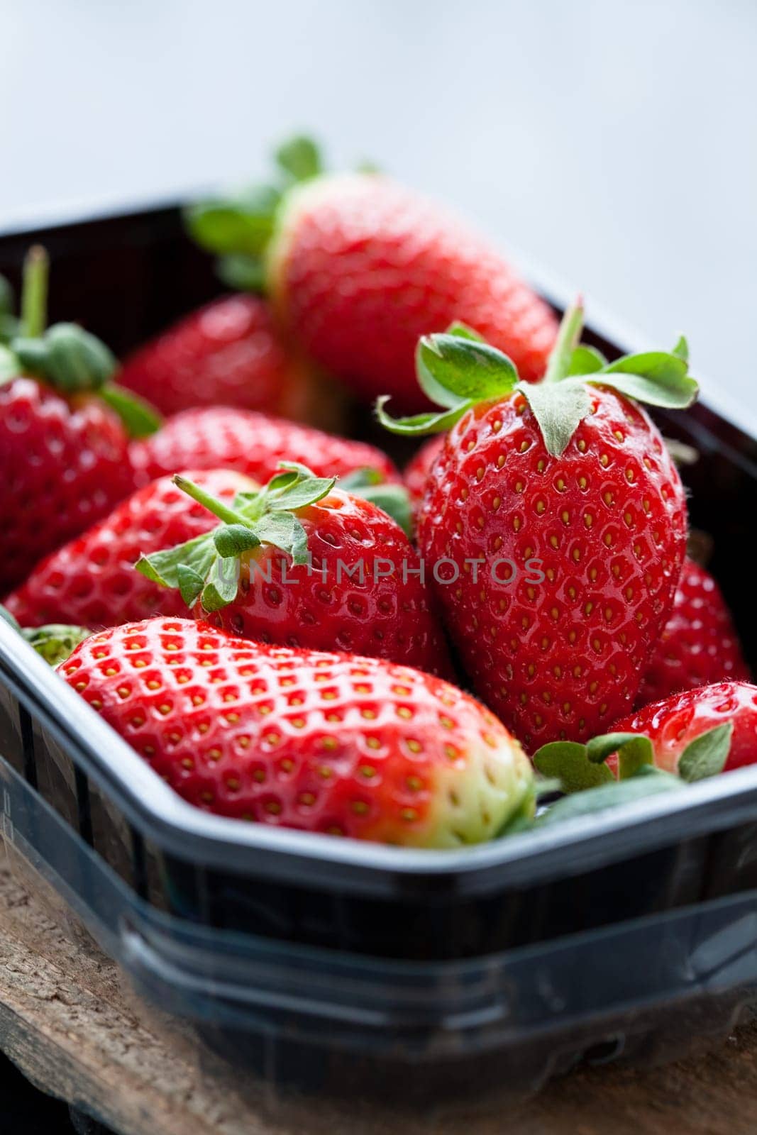 Fresh whole strawberries in plastic packing tray on wooden surface
