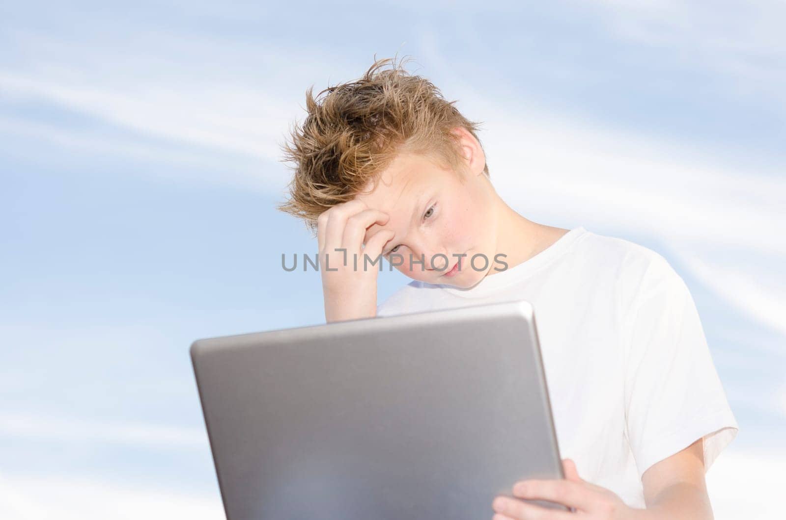 High key portrait of teenager with laptop against blue sky background
