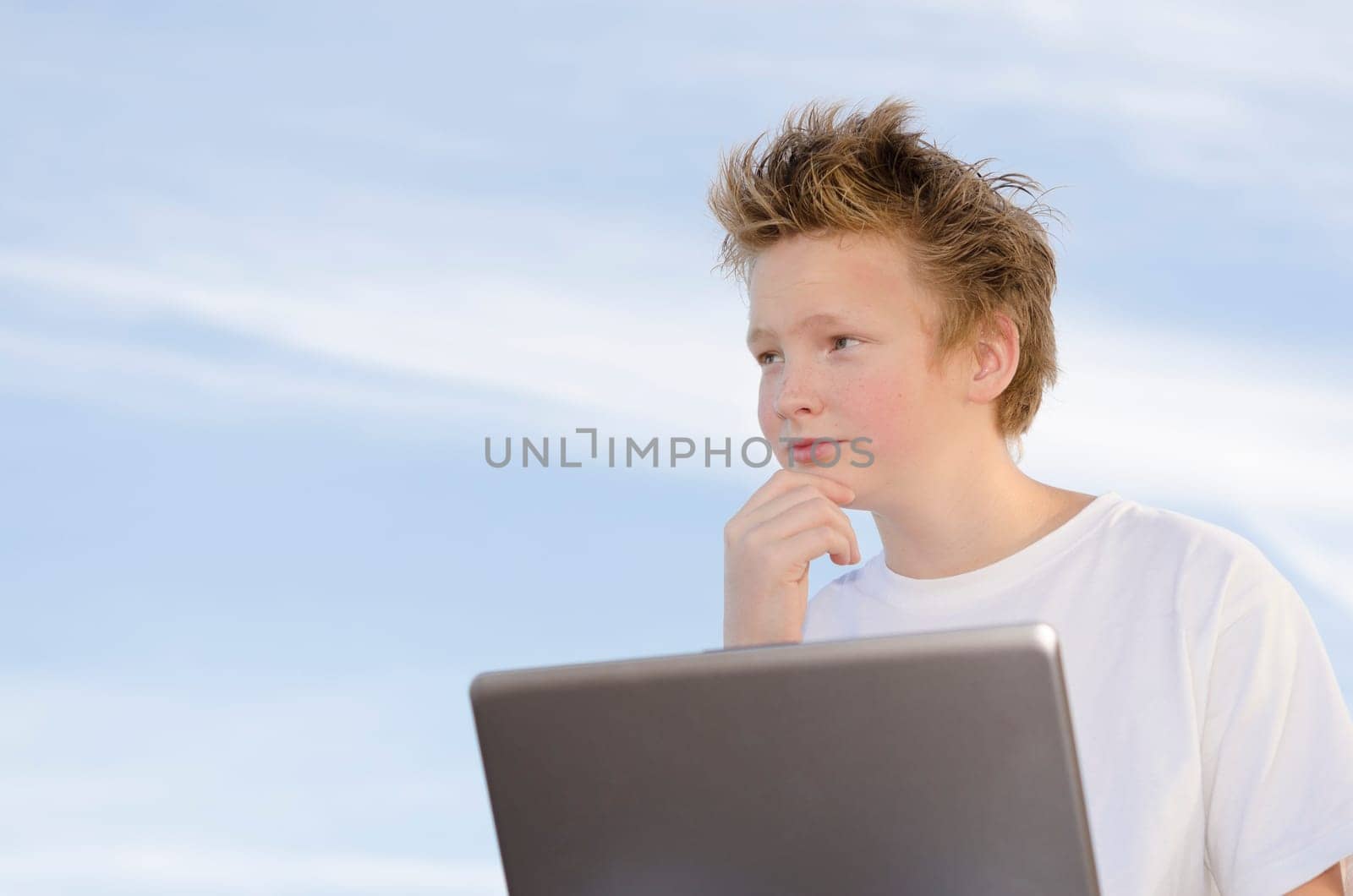 Serious schoolboy with mobile computer think about something on nature