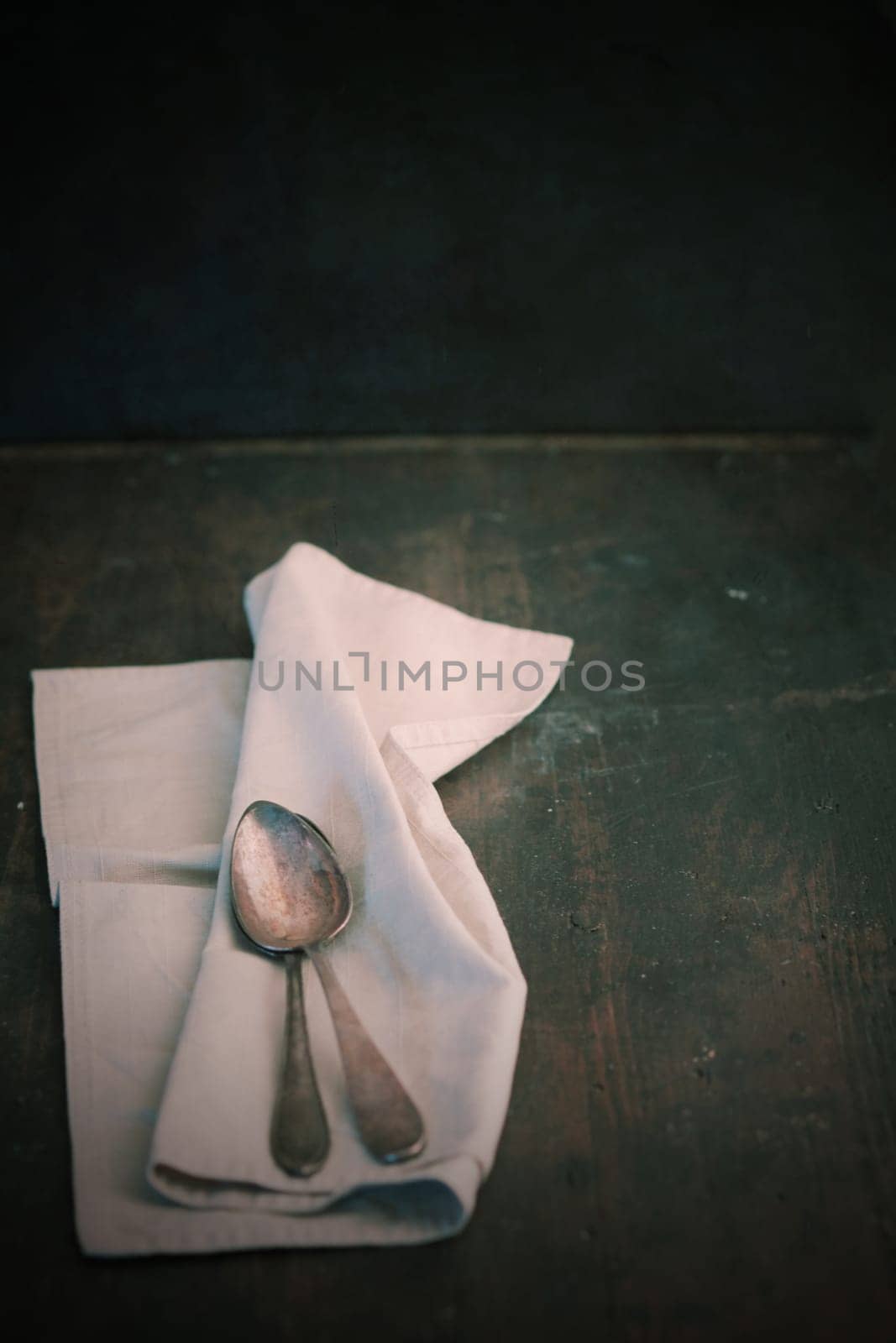 Folded plain white linen napkin and teaspoons on an old dark wooden table with copyspace