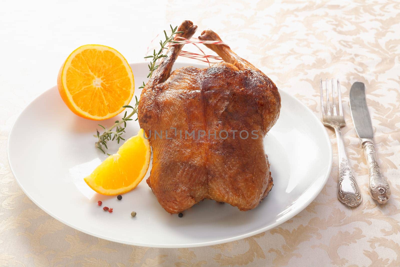 Golden crisp roast chicken or duck served whole on a plate accompanied by sliced orange and rosemary