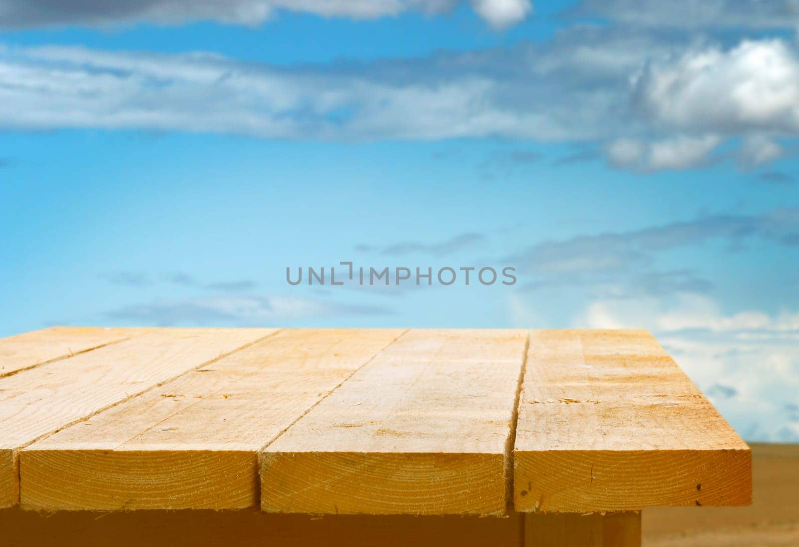 Empty wooden table top against a blue sky with fluffy white clouds for the placement of your food or product