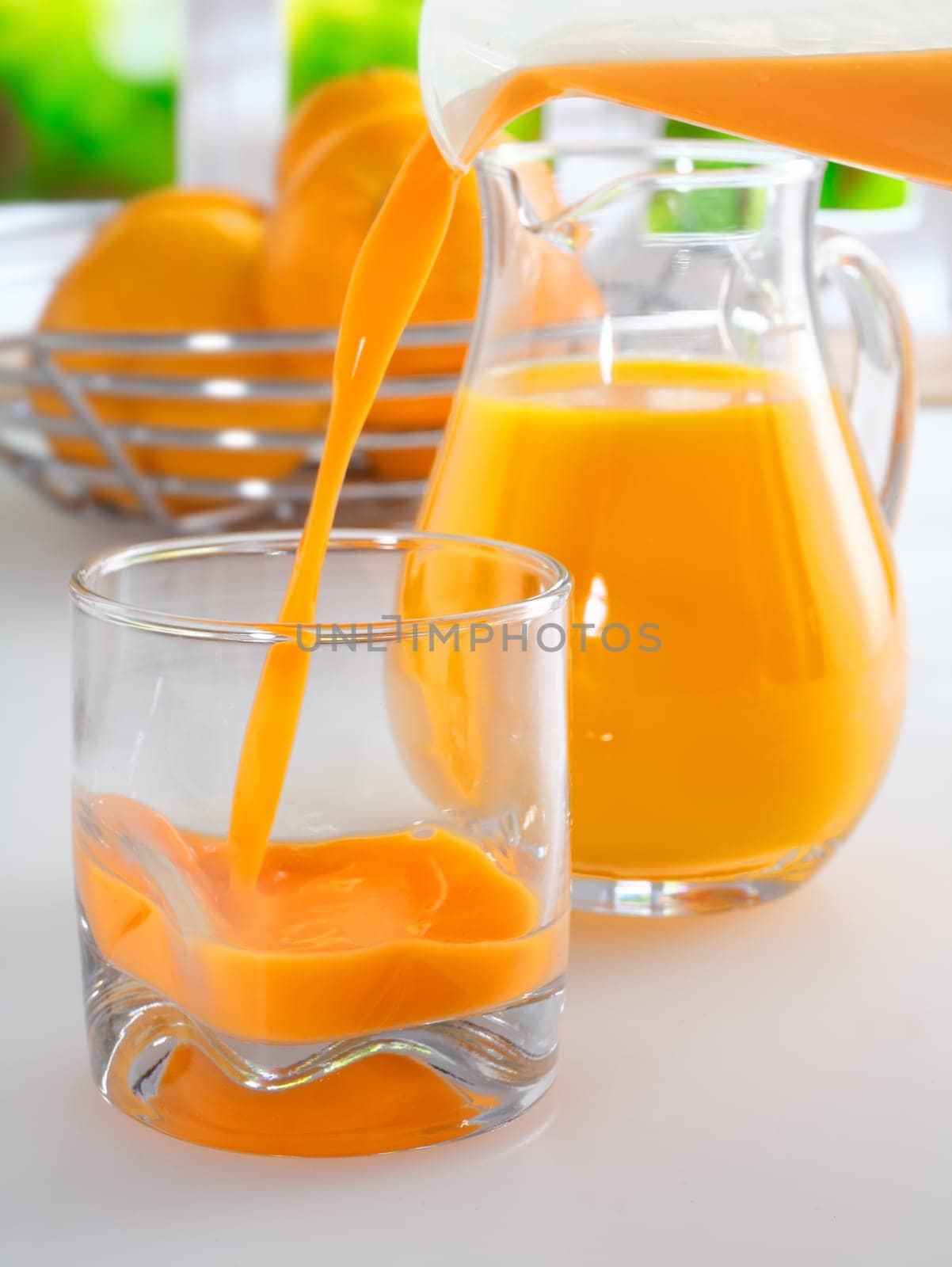 Pouring a glass of fresh healthy orang juice from a jug with a full glass pitcher of juice standing ready in the background