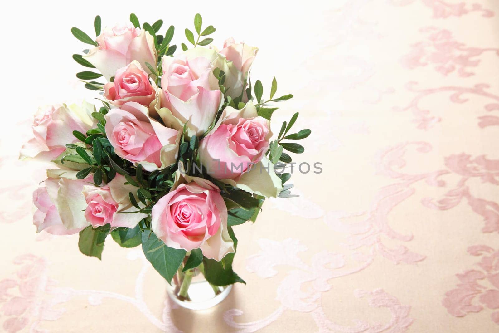 High angle view of a bouquet of fresh pink roses with greenery arranged in a glass vase with copyspace