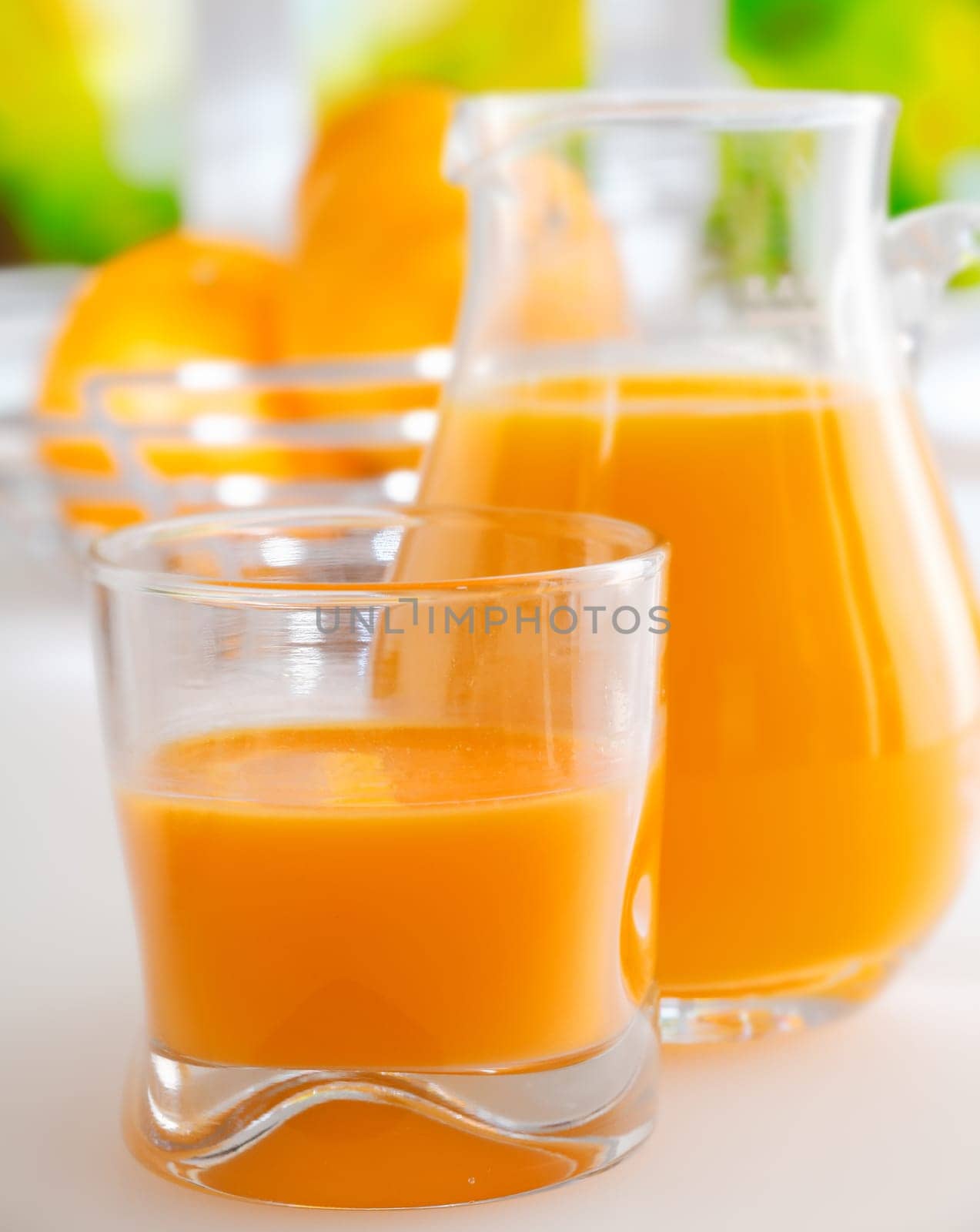 Glass and jug of vibrant colourful healthy fresh orange juice standing on a kitchen table ready for breakfast