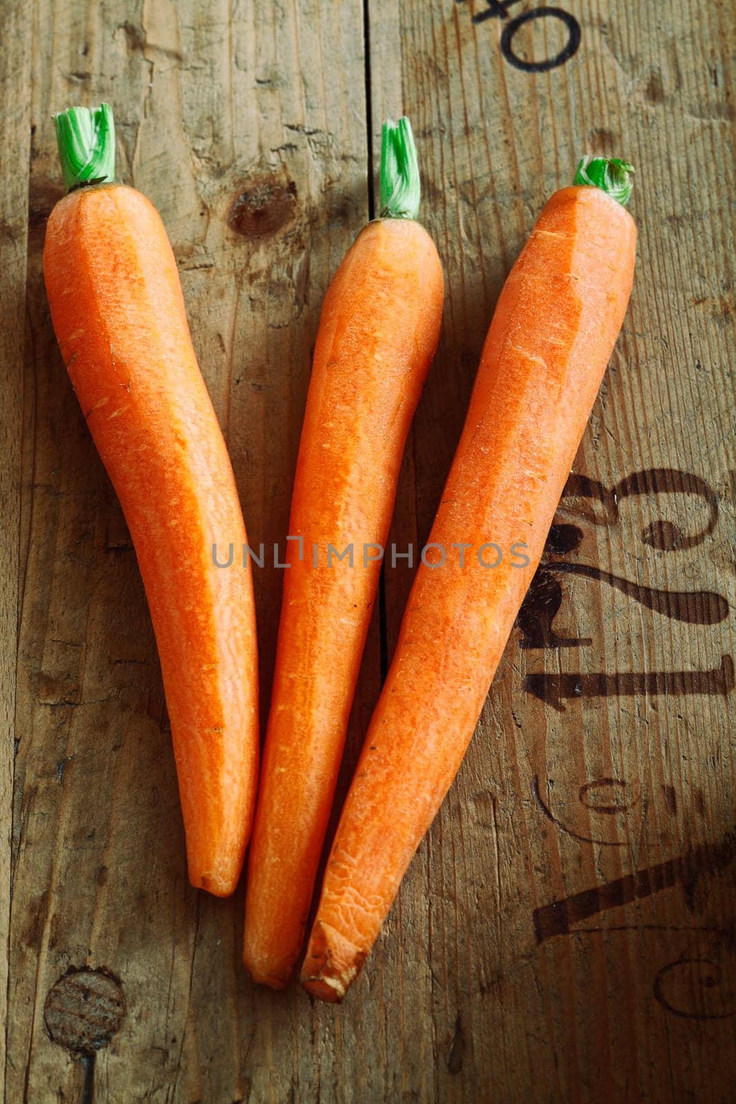 A trio of trimmed fresh carrots on rustic wooden packing crate background