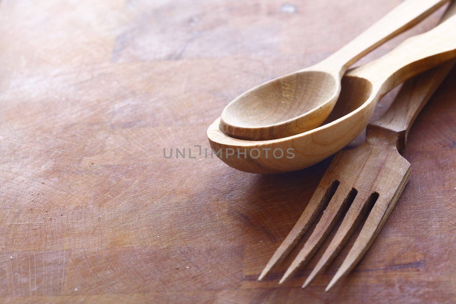 Handcrafted wooden kitchen utensils with a fork and spoons in two sizes lying on a wood surface with copyspace