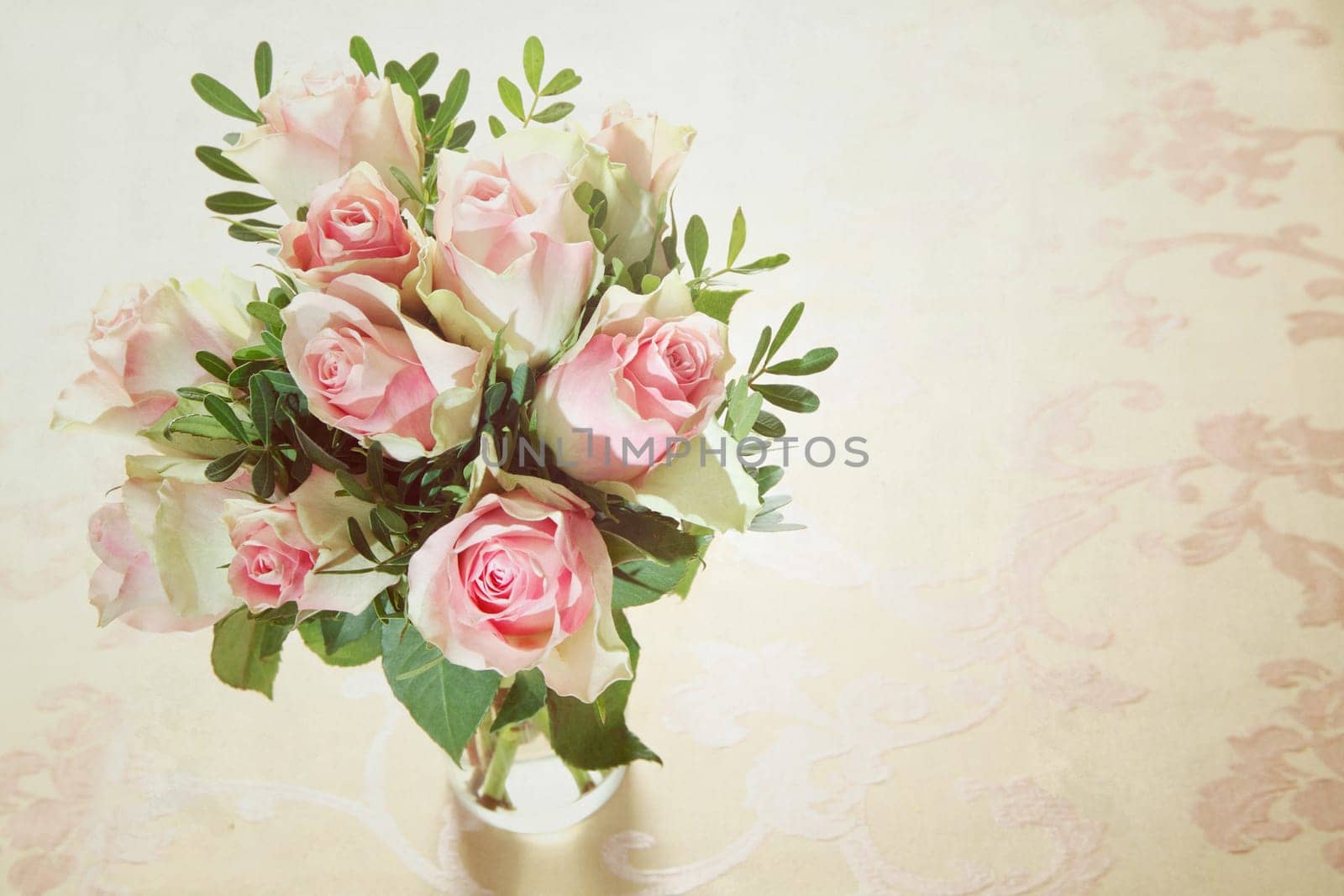High angle view of a bunch of delicate fragrant fresh pink roses arranged in a glass vase with greenery and copyspace