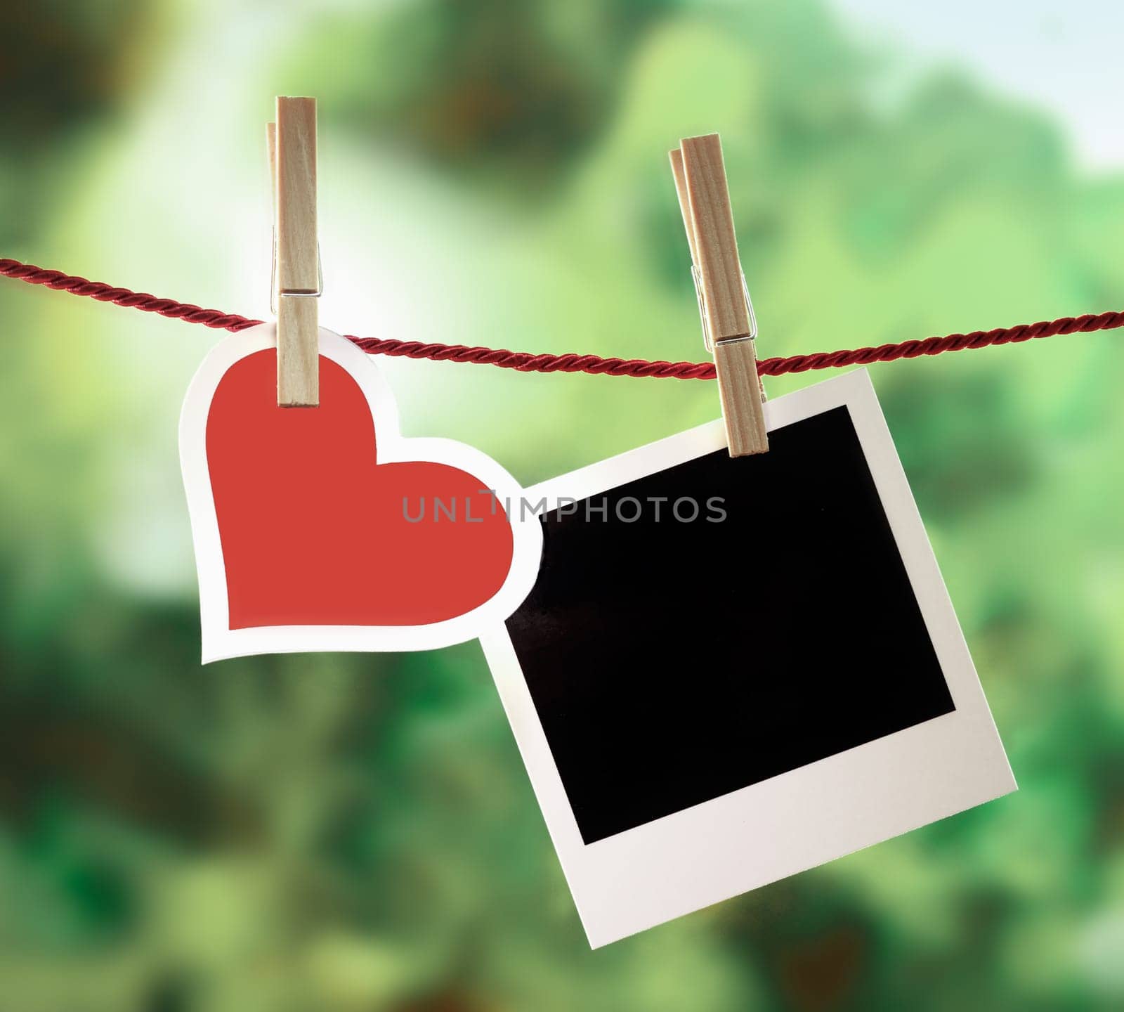Romantic Valentine memories and greeting card with a pretty white-bordered red heart hanging on an outdoor line with a blank instant photo frame for your image or message