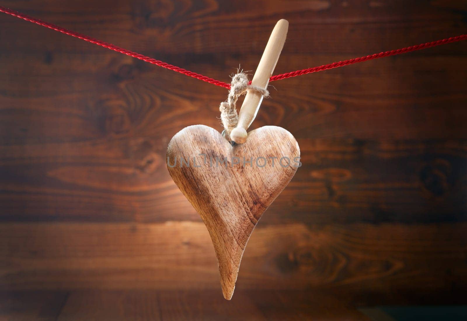 Rustic Valentines greeting card with an elegantly shaped handcrafted wooden textured heart hanging from a peg on a string against a woodgrain timber background with vignetting