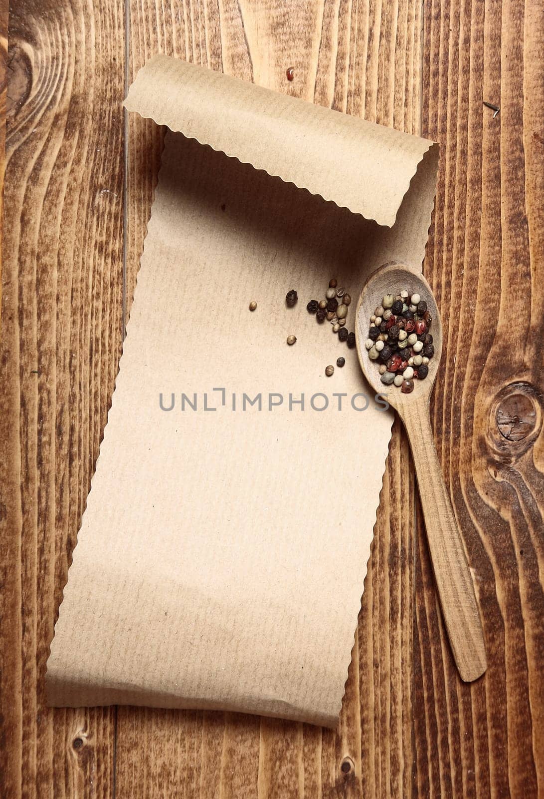 Brown paper on wood with a wooden spoon and peppercorns