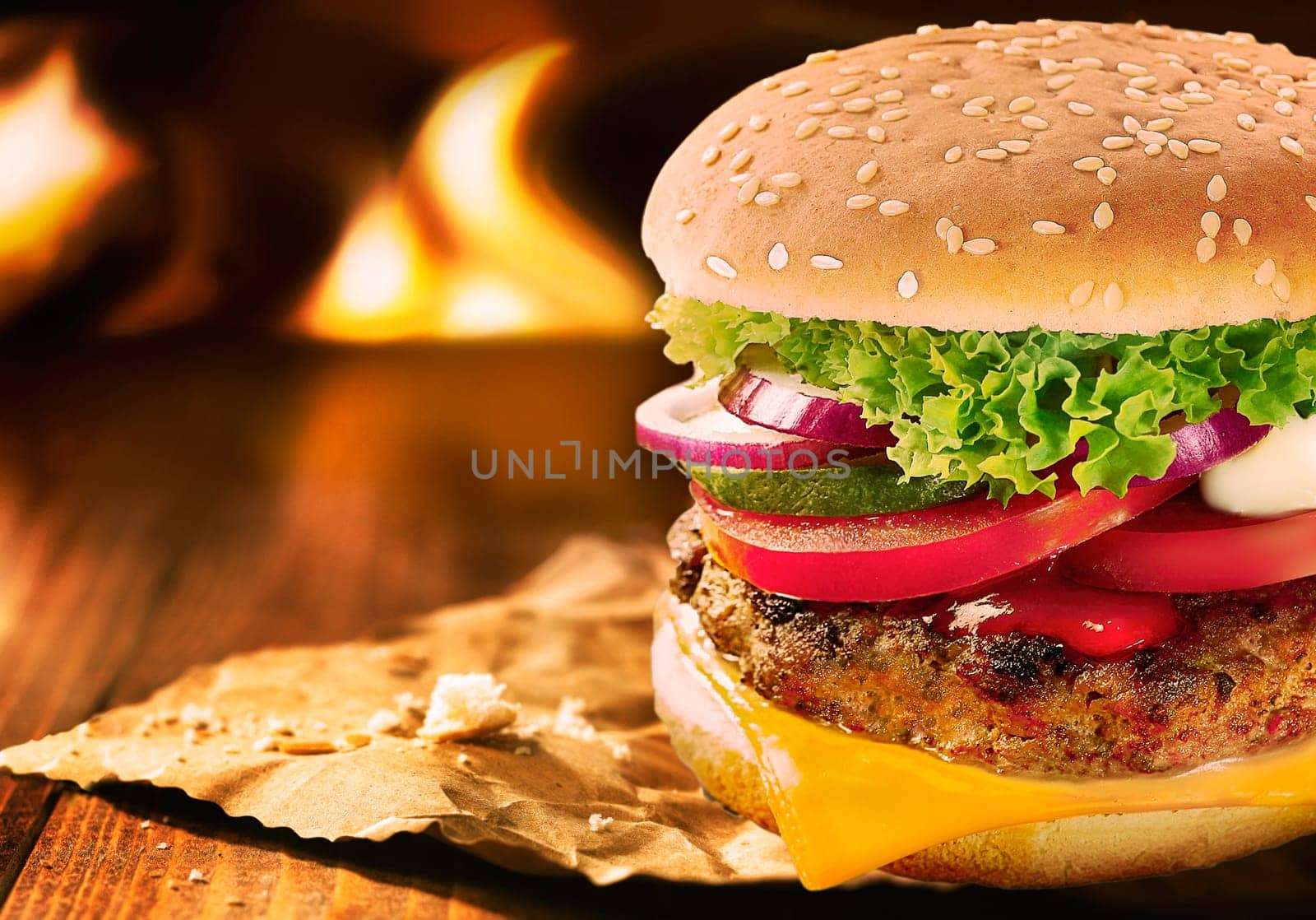 Delicious whopper cheese burger with beef patty, cheddar cheese and fresh salad ingredients on a sesame bun served on a wooden table near an open fire