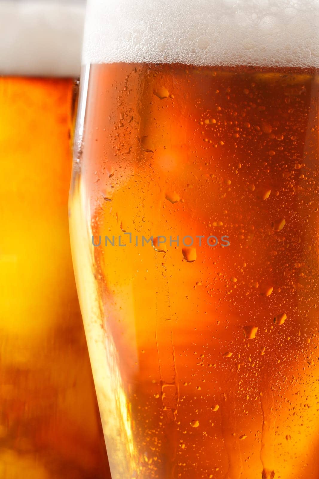 Cropped closeup of a glass of cold beer with a frothy head and water droplets from condensation beading the outside of the glass
