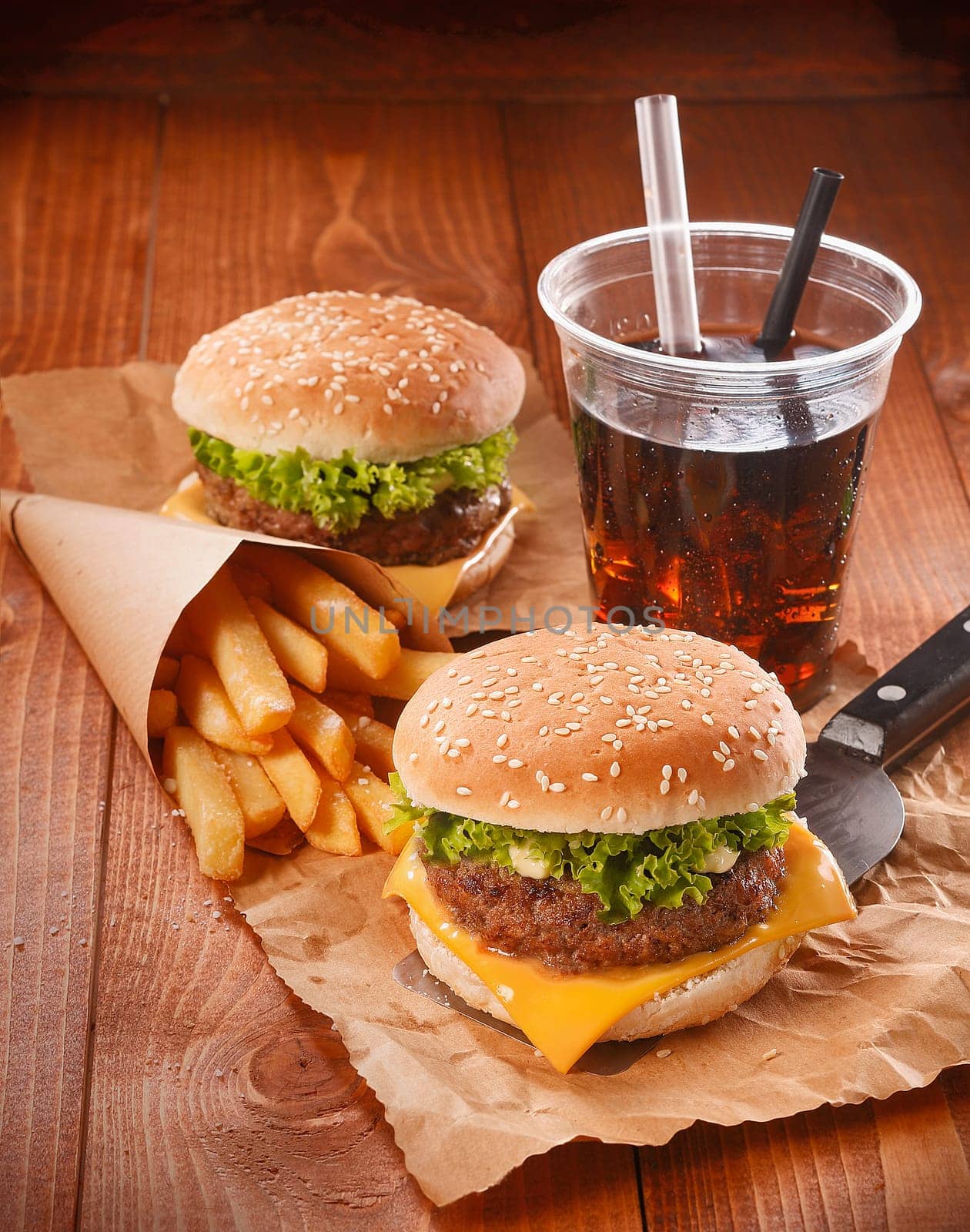 Two hamburgers and fries on brown paper with glass of softdrink