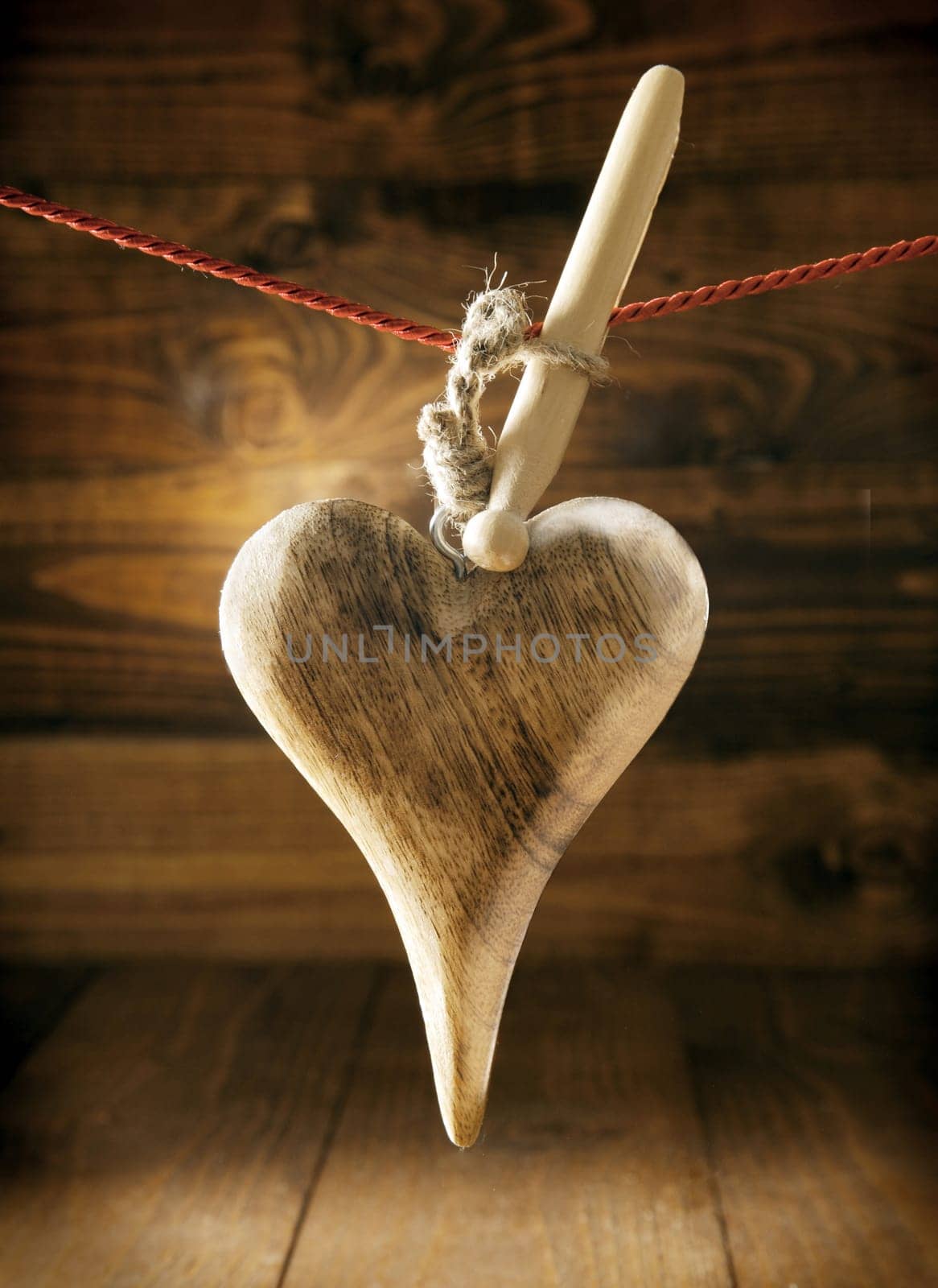 Handcrafted rustic wooden textured heart with woodgrain hanging on a string and peg against a timber backdrop for a simple Valentines or anniversary greeting card
