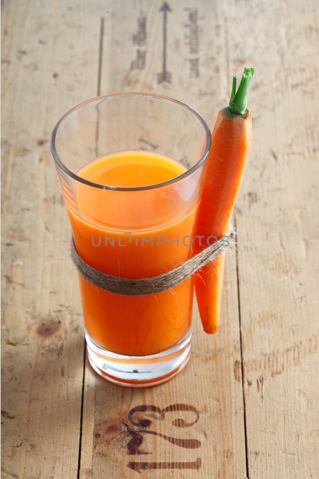 Fresh vegetarian carrot juice blend in a tall glass on an old wooden surface with stamped numbers with a whole carrot tied to the side