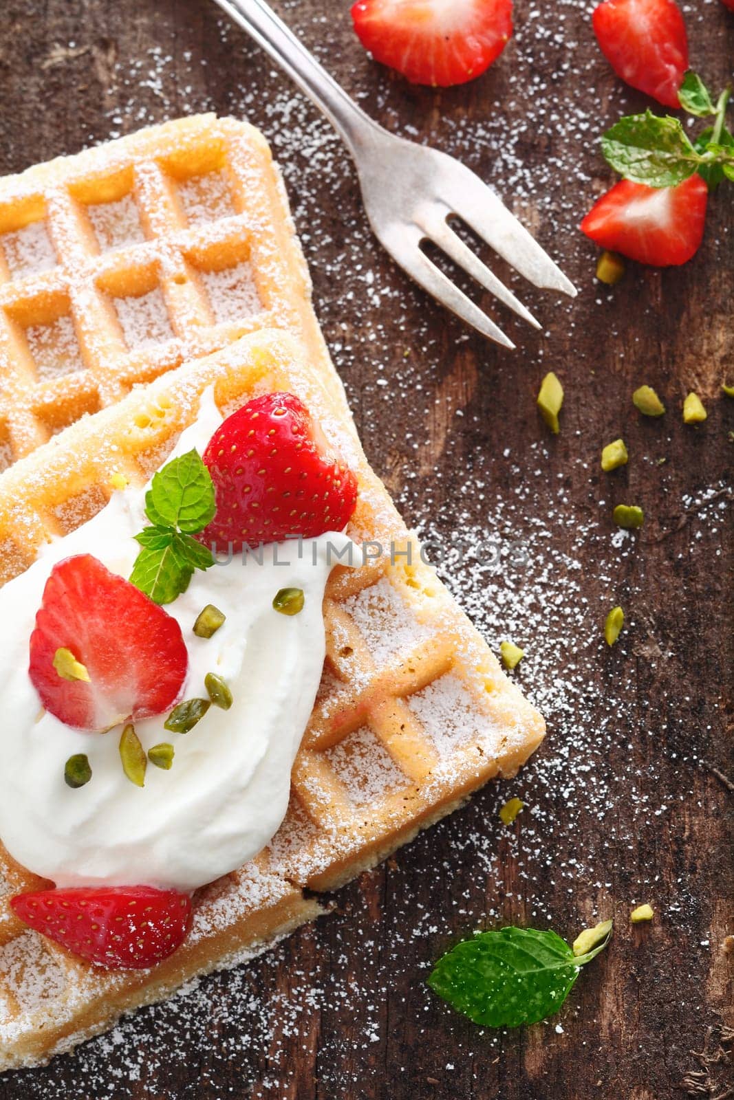 Crisp golden waffle topped with strawberries and whipped cream and garnished with mint on a rough wooden table top
