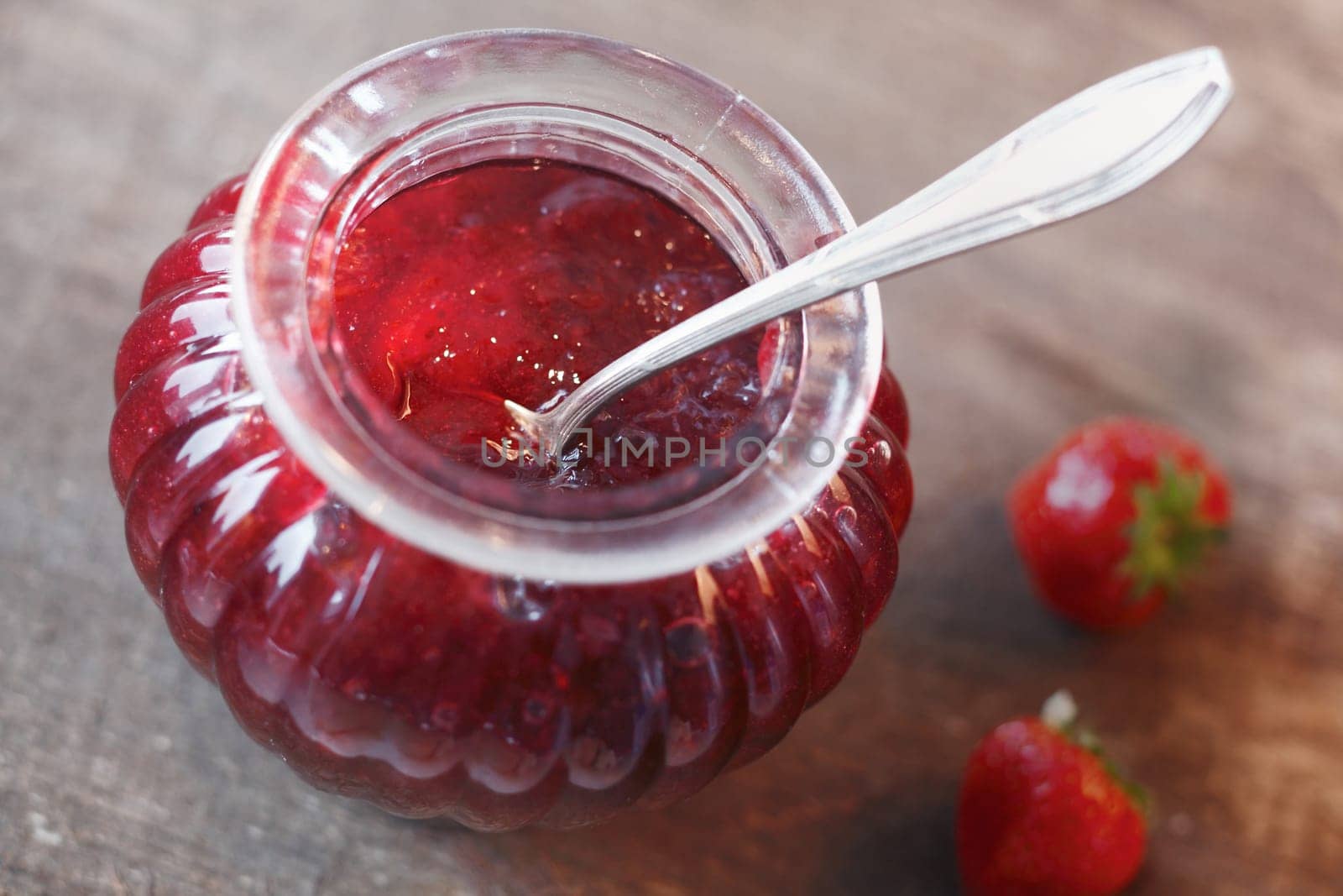 Overhead view of a glass jar of fresh homemade strawberry preserve or jam with a silver teaspoon resting inside