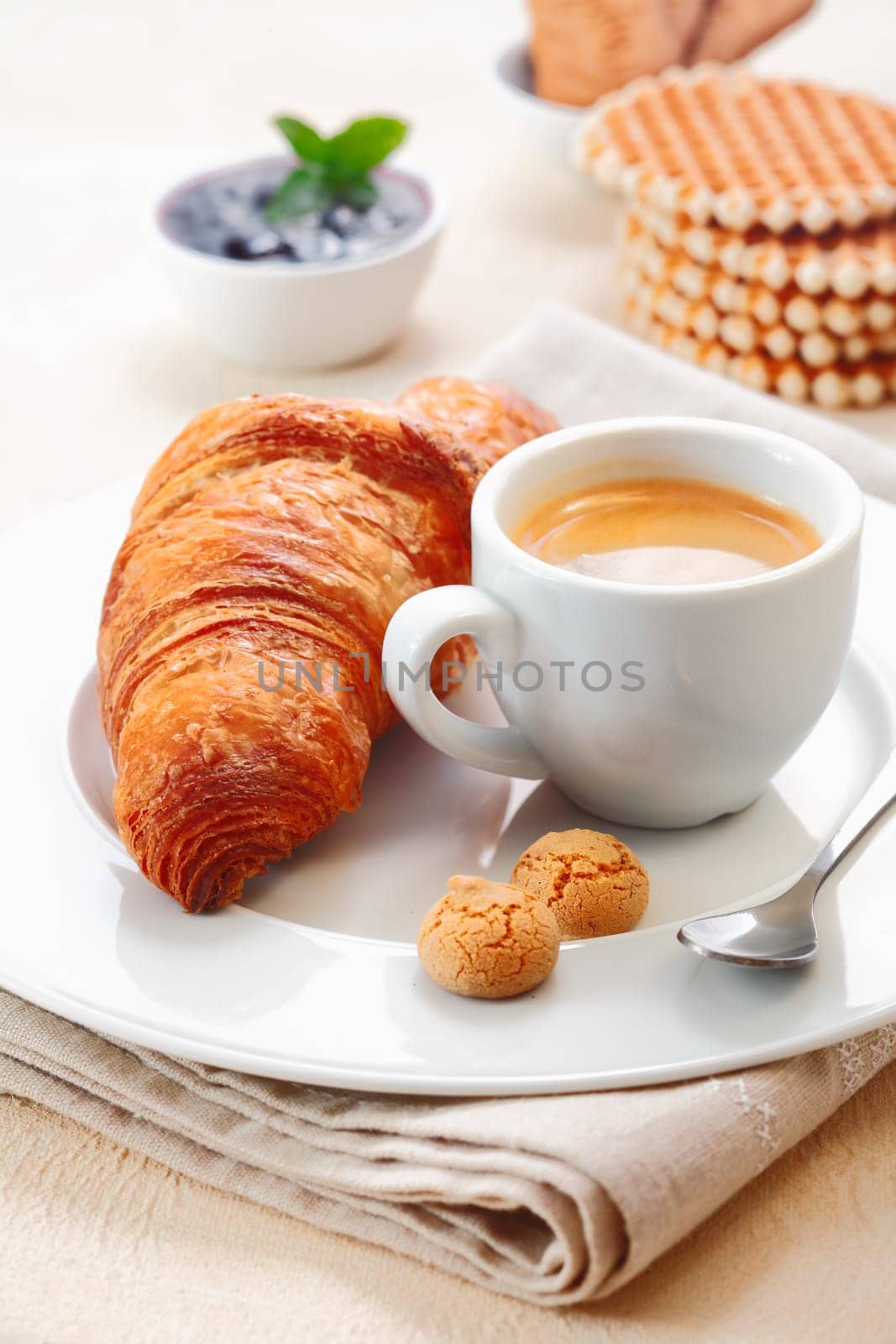 Freshly baked crisp golden croissant served with a cup of rich espresso and two small macaroon biscuits in a restaurant