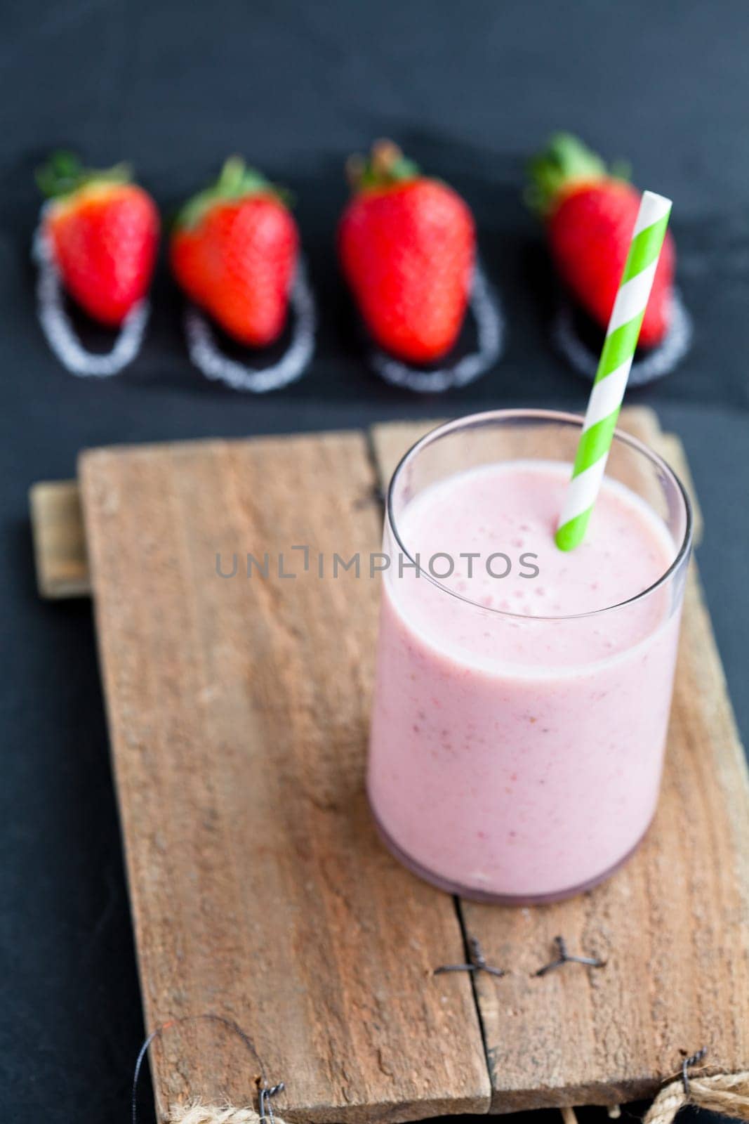Strawberry smoothie with striped straw and whole strawberries on dark background