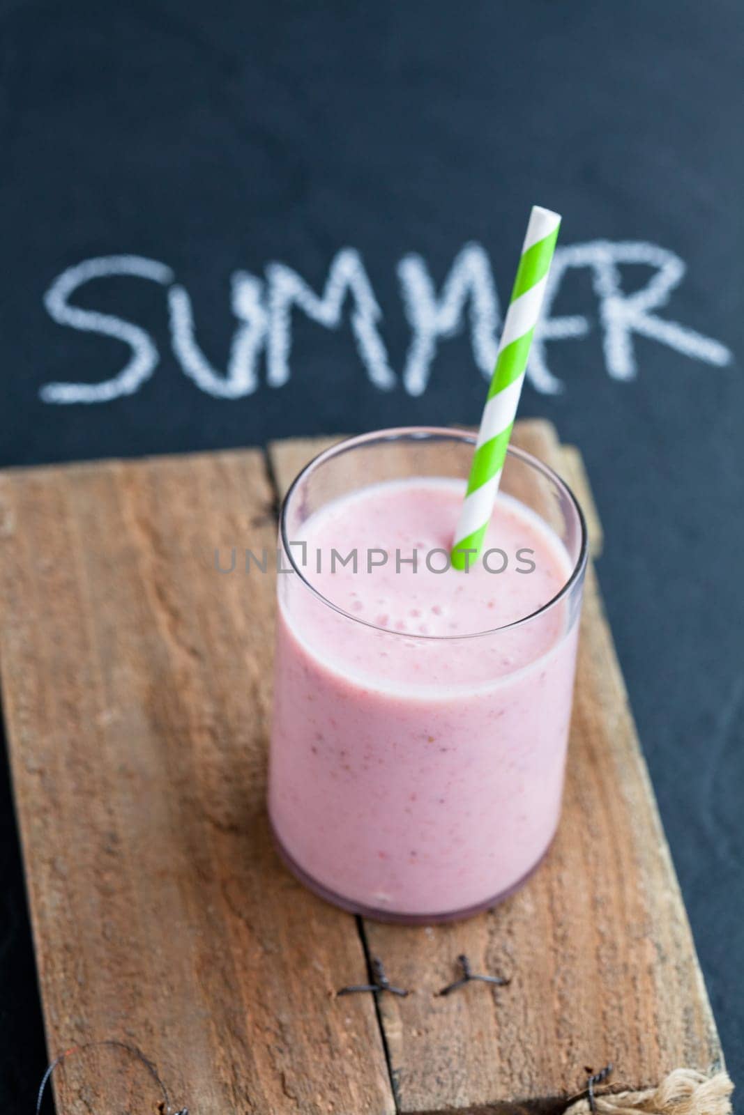 Strawberry smoothie with striped straw on wooden serving tray
