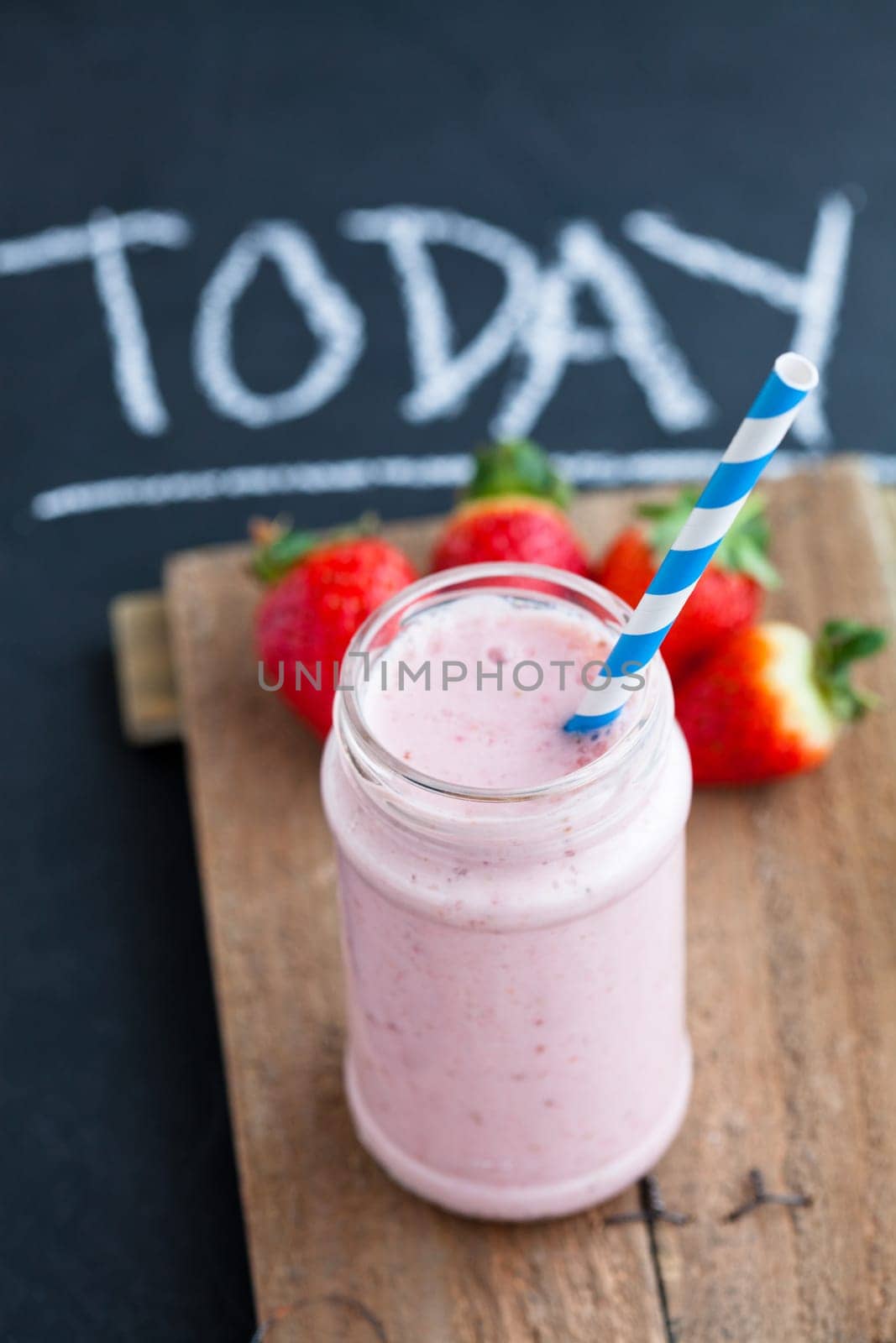 Strawberry smoothie with striped straw and whole strawberries on wooden serving tray